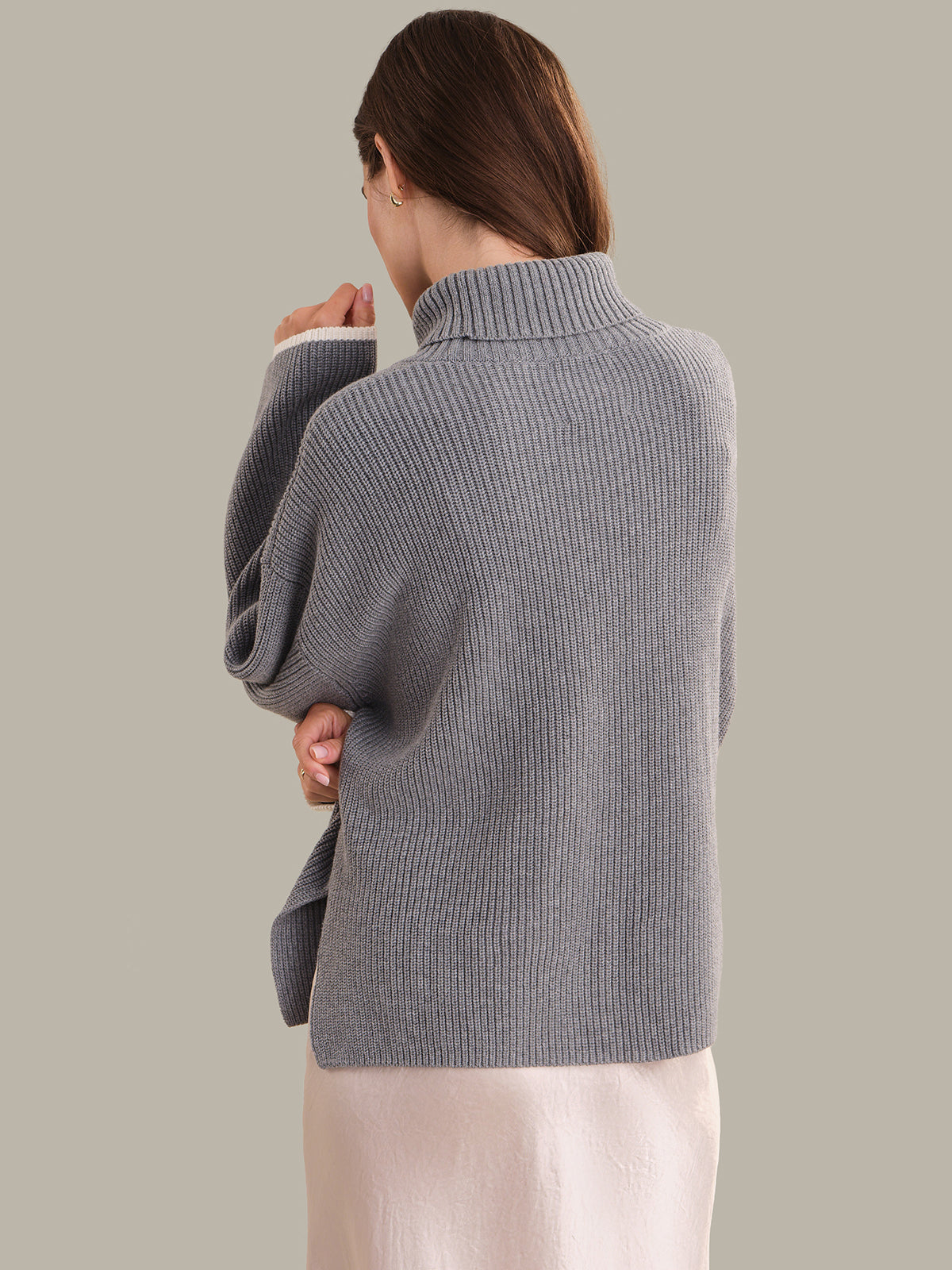 Person wearing a gray ribbed sweater against a plain background