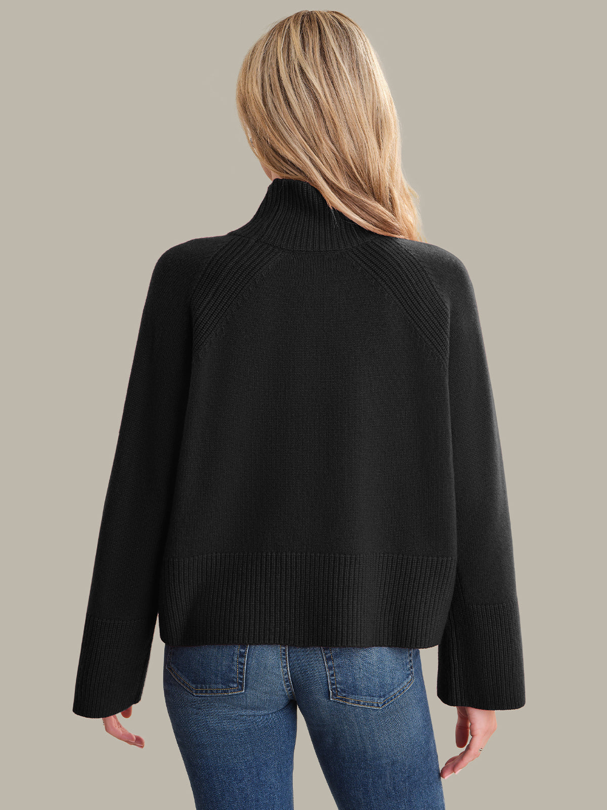 Person wearing a black sweater and blue jeans on a plain background