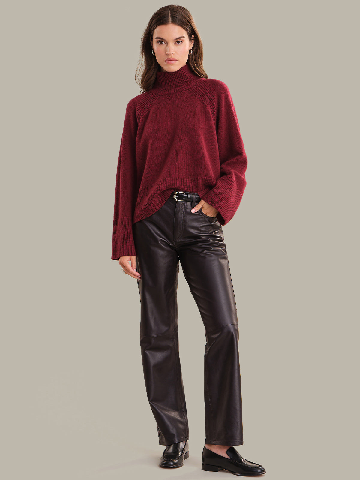 Woman wearing a burgundy sweater and black leather pants on a gray background