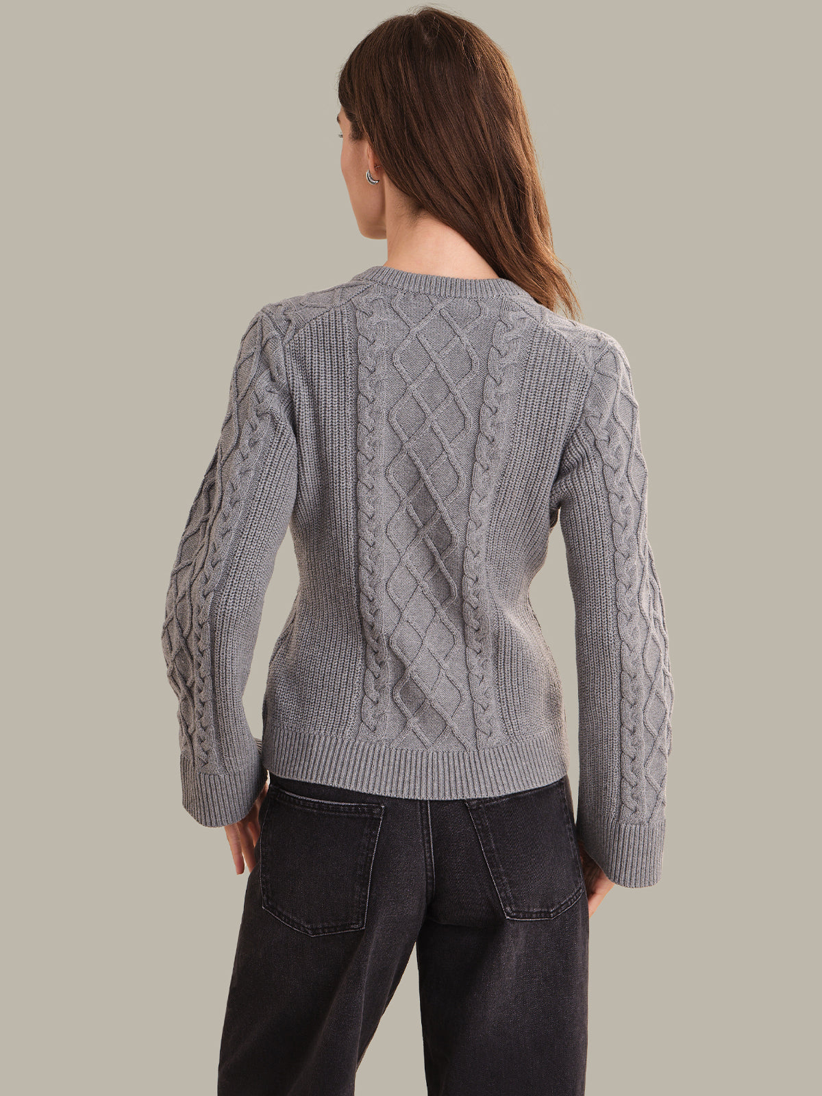 Person wearing a gray cable knit sweater against a plain background