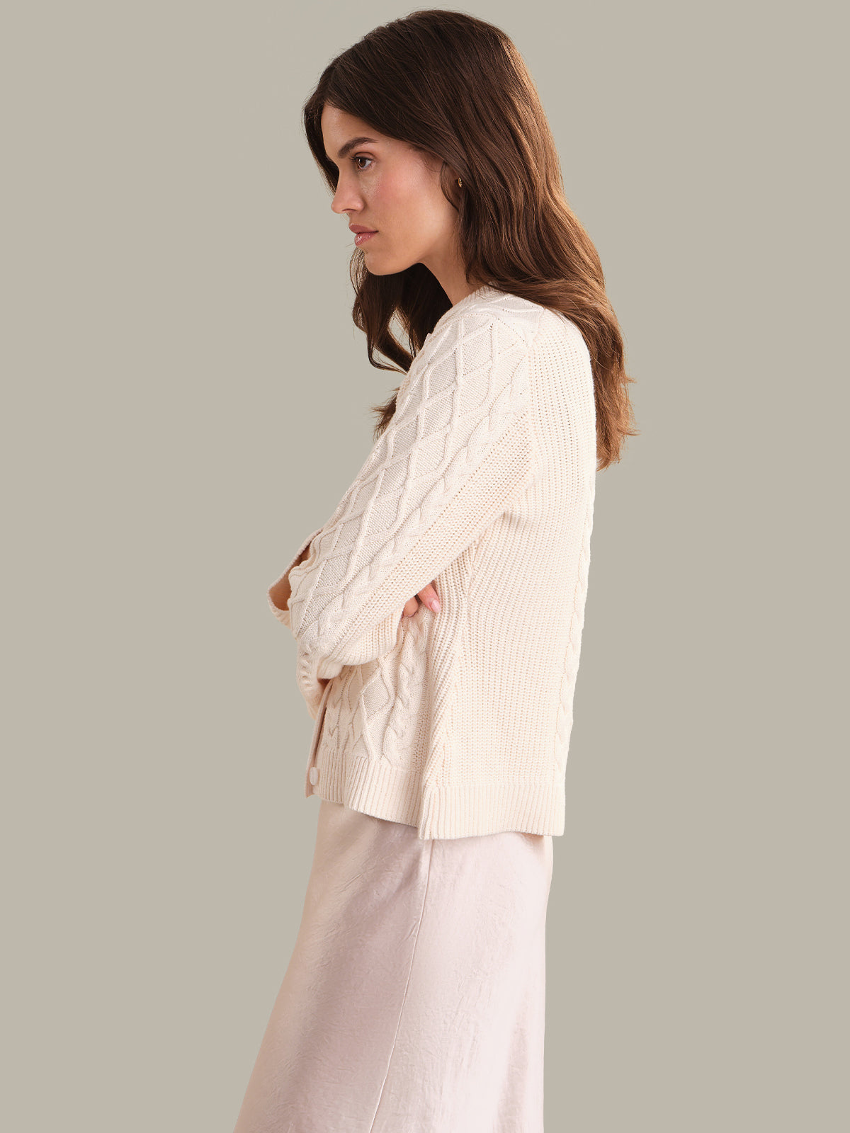 Woman wearing a cream-colored cable knit cardigan against a neutral background