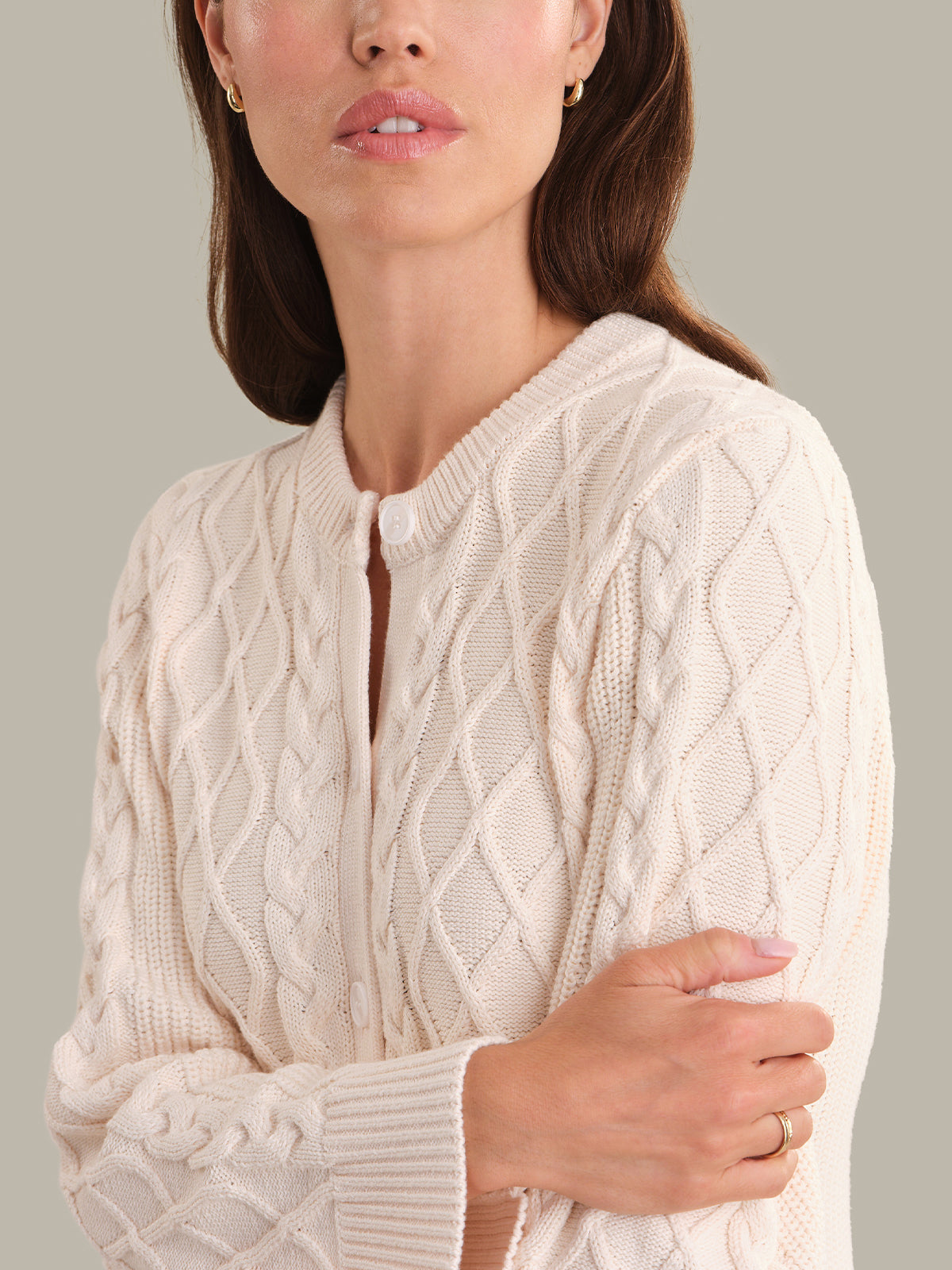 Woman wearing a cream cable knit cardigan against a neutral background
