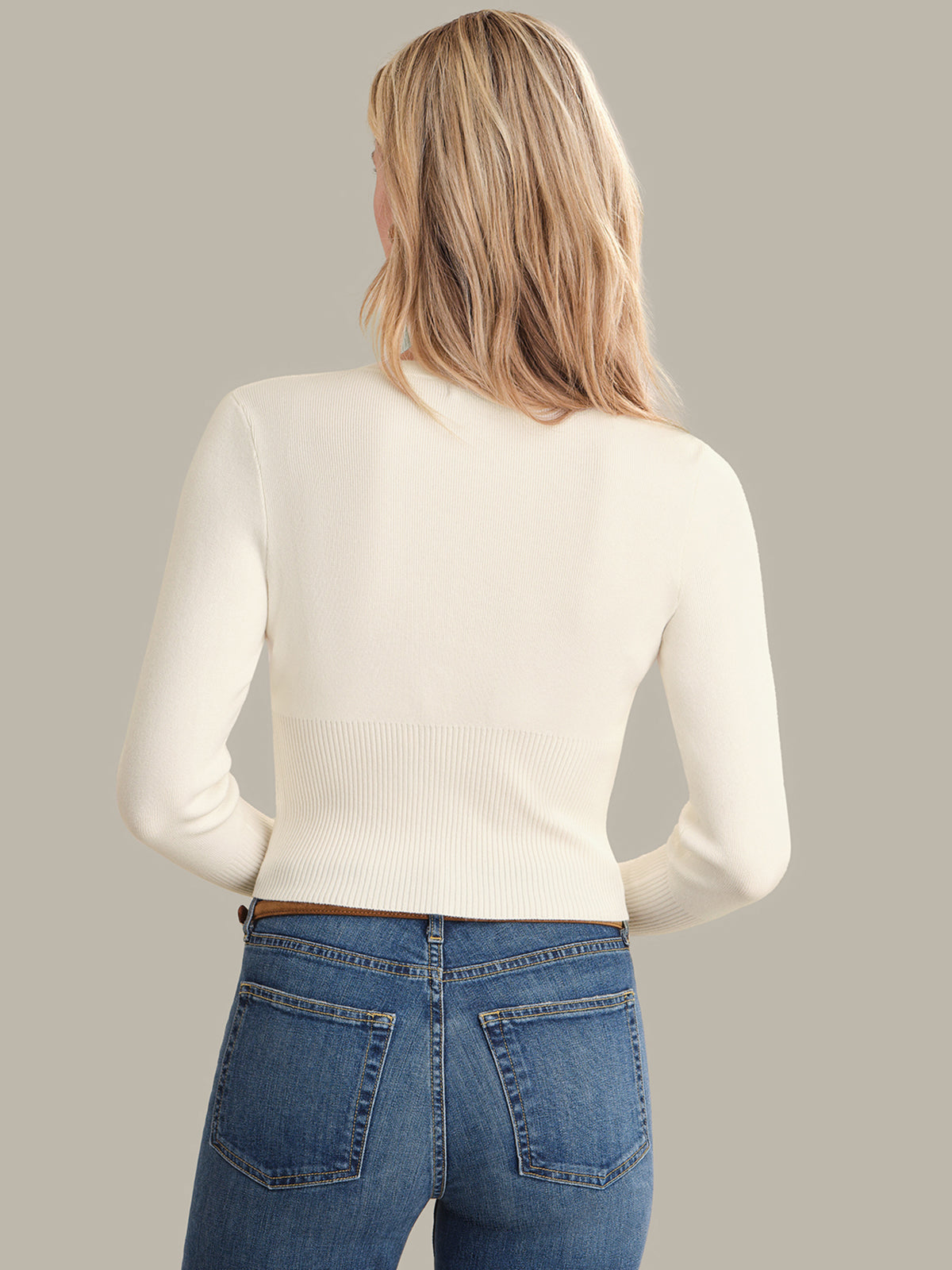 Person wearing a white sweater and blue jeans on a neutral background