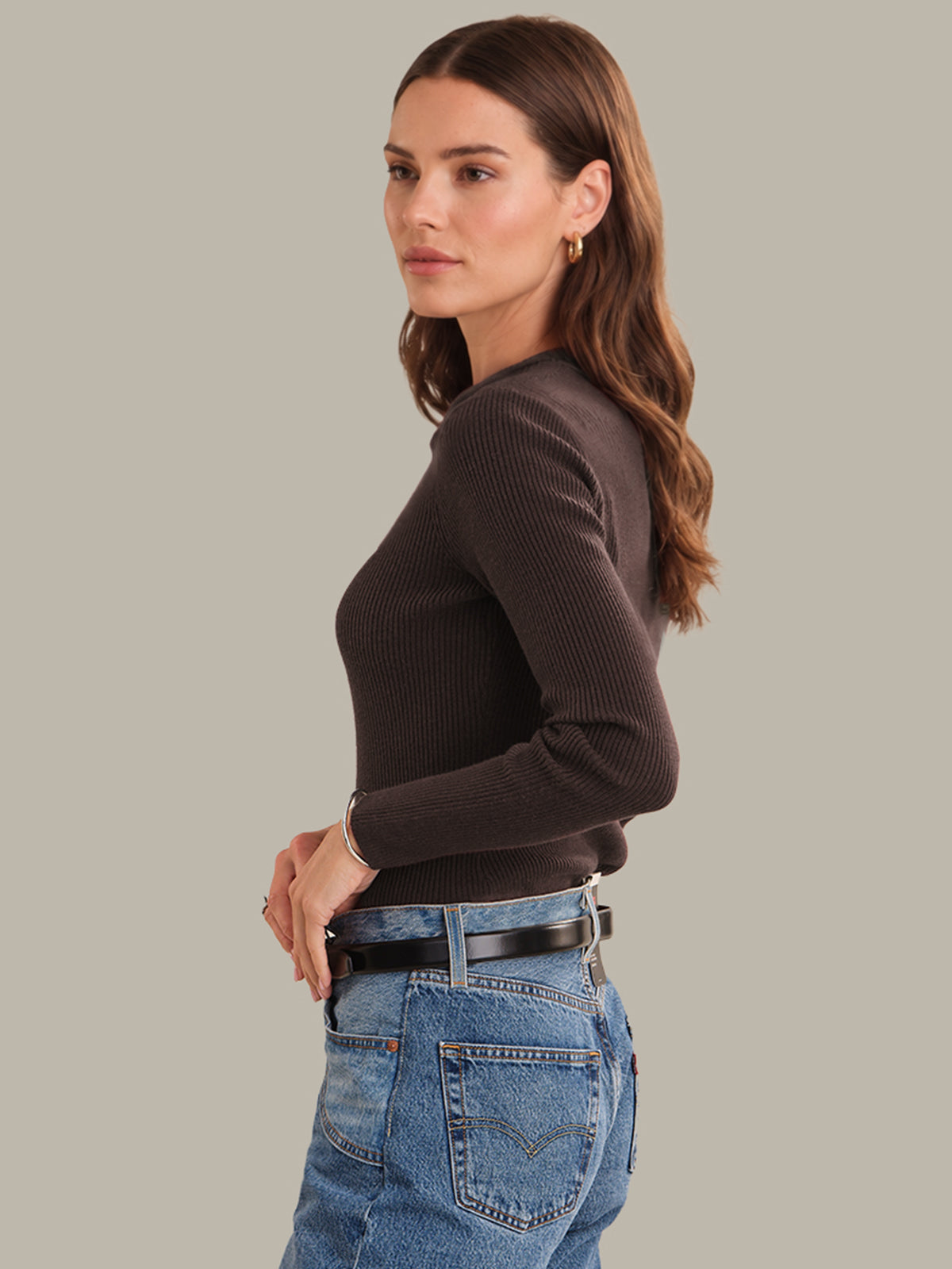 Woman wearing a brown ribbed sweater and blue jeans on a gray background