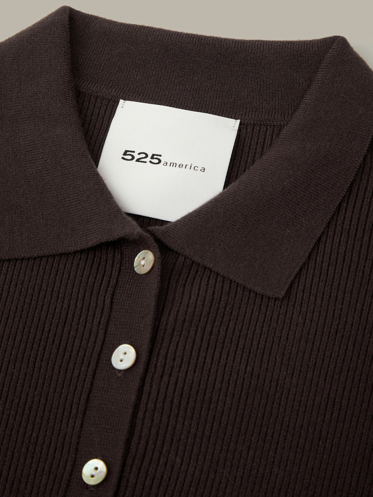 Close-up of a brown ribbed sweater with a brand label on a neutral background