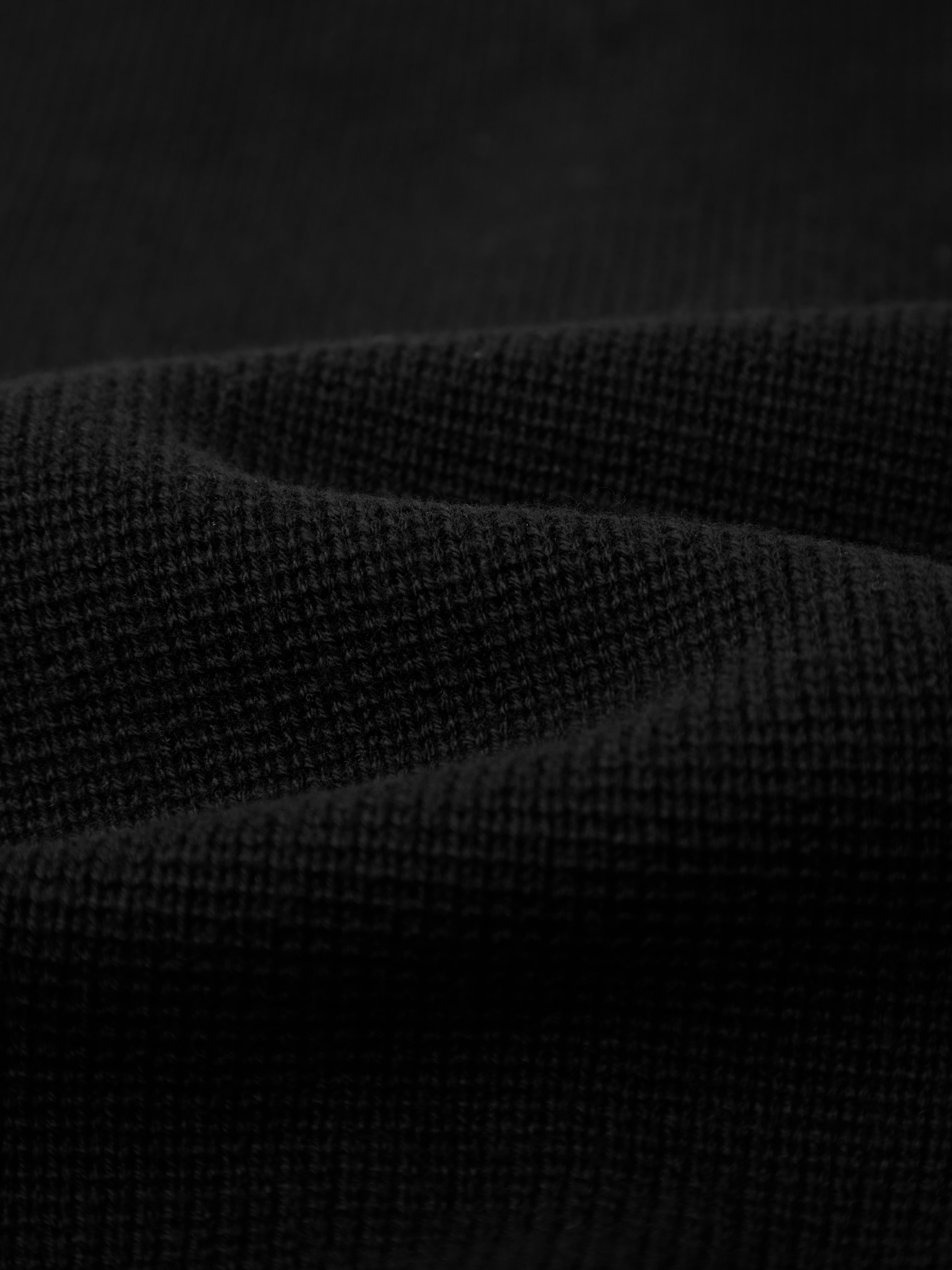 A close-up of pure cotton black fabric with a grid pattern and soft texture, highlighting the weave—ideal for a stylish wardrobe staple such as 525 America’s Crewneck Cotton Cardigan.