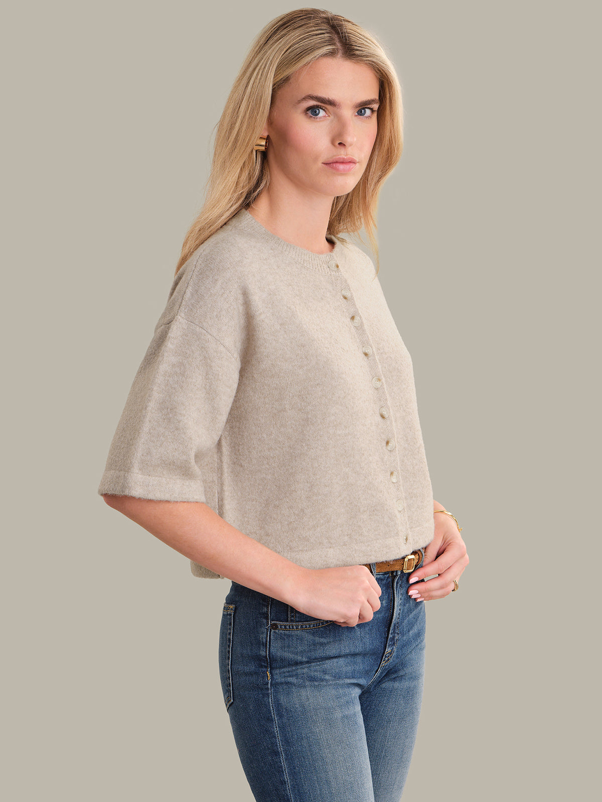 Woman wearing a beige short-sleeve cardigan and blue jeans against a gray background