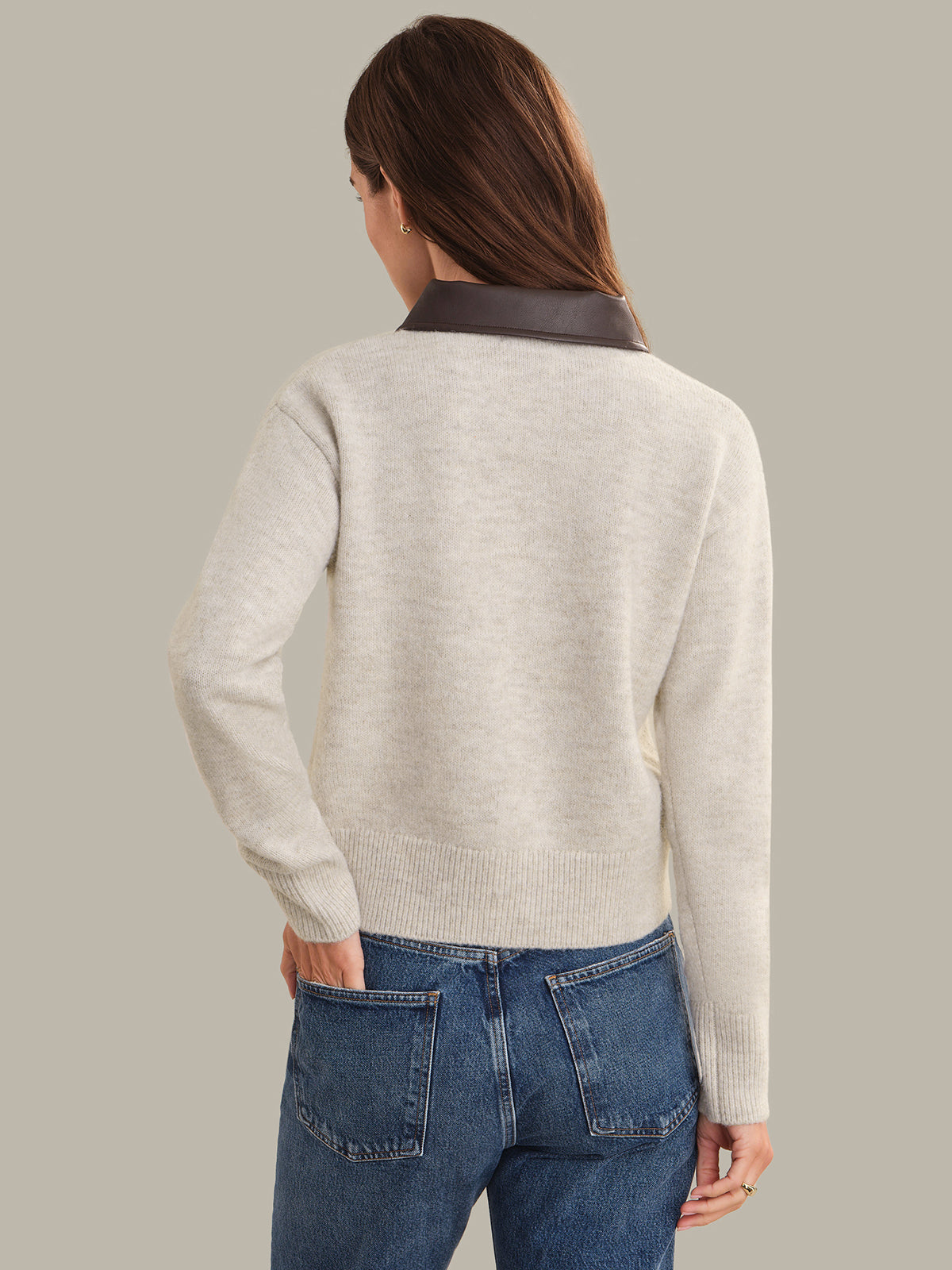 Person wearing a light gray beige and blue jeans on a plain background