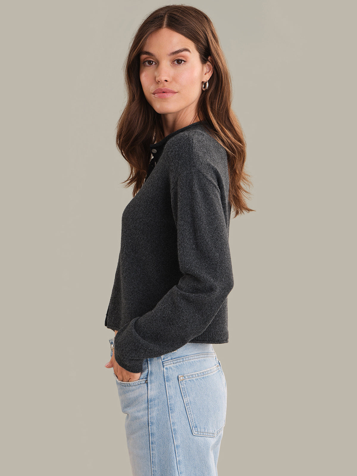 Woman wearing a dark gray sweater and light blue jeans against a plain background