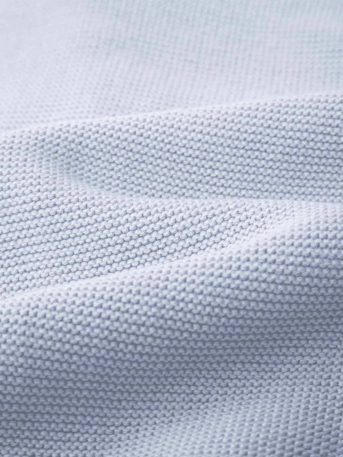 Close-up of 525 America’s light blue knit fabric with a textured surface and visible horizontal stitches, featuring gentle folds and soft shadows—ideal for layering under pieces with a classic crew neckline.