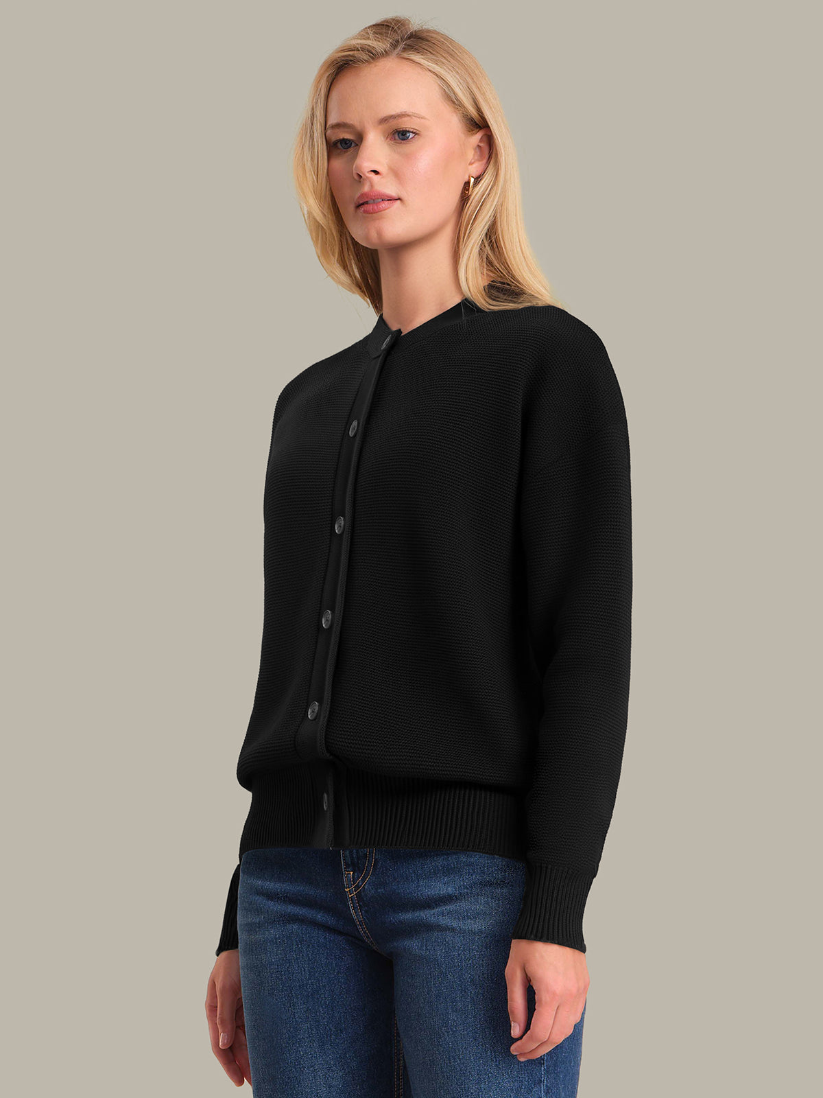 Woman wearing a black cardigan and blue jeans against a plain background