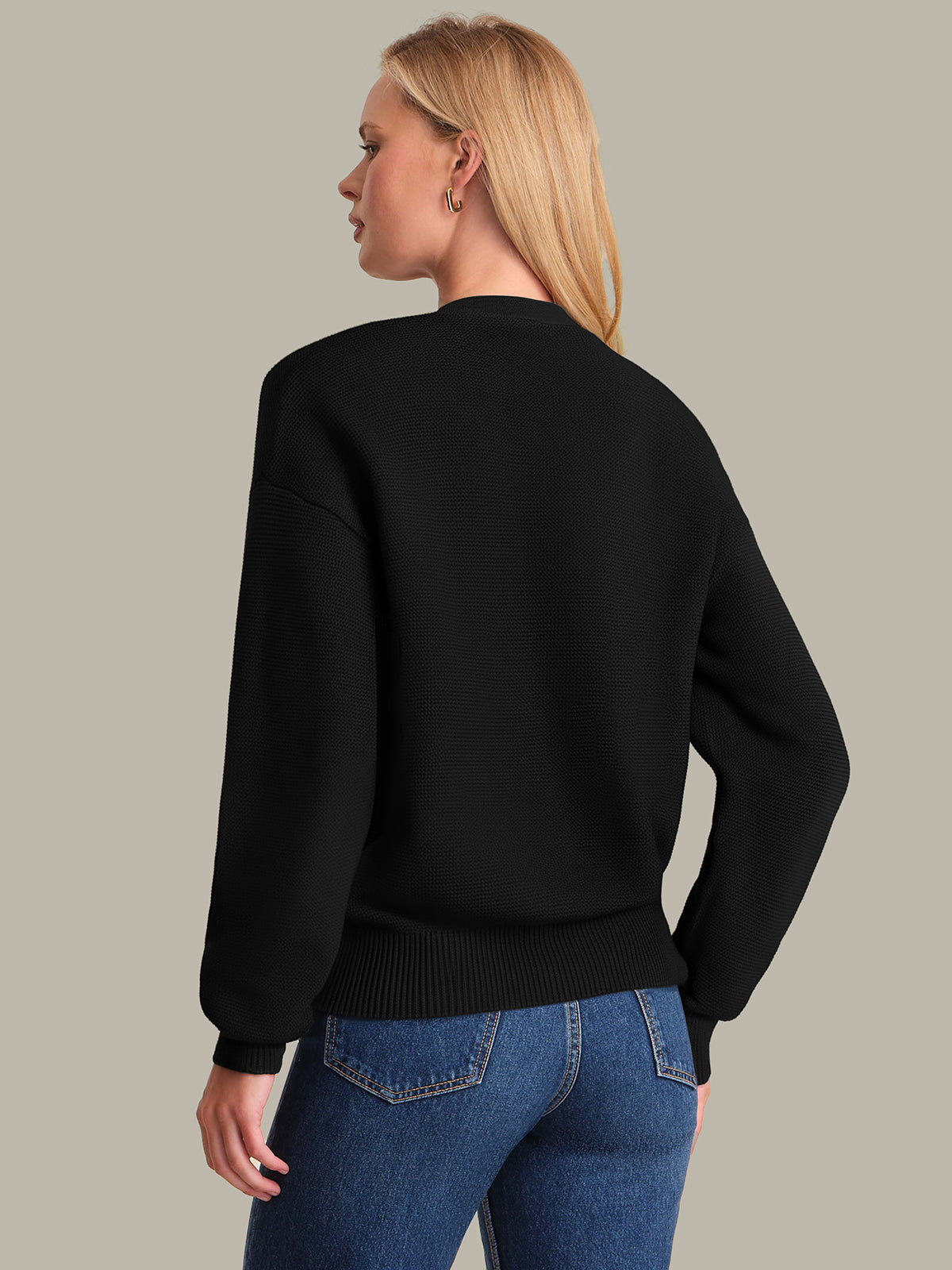 Person wearing a black sweater and blue jeans on a beige background