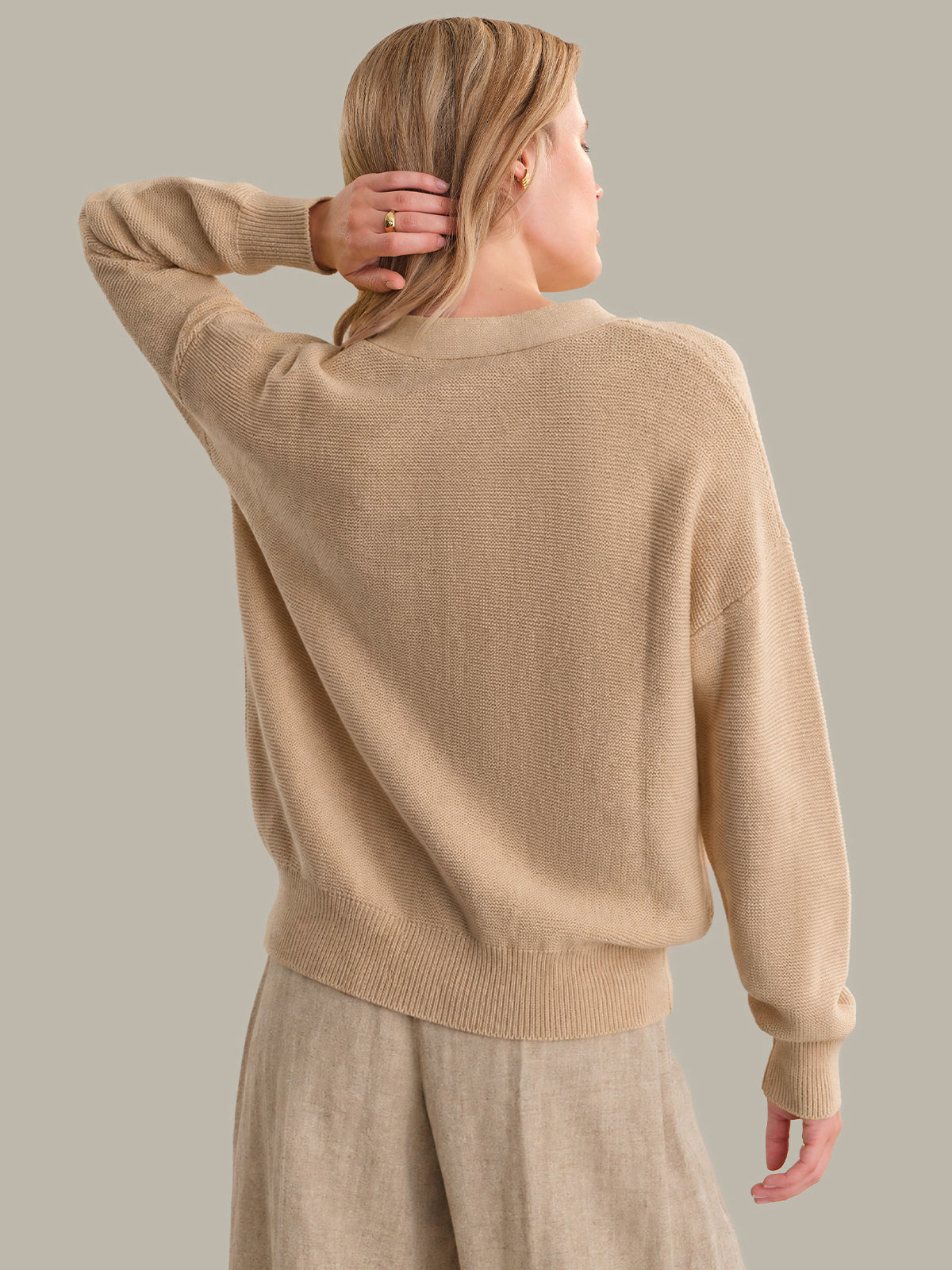 Person wearing a beige cardigan and pants against a neutral background