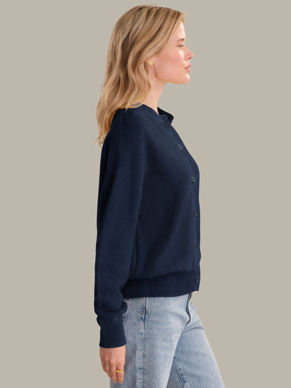 Woman wearing a navy cardigan and light blue jeans against a plain background