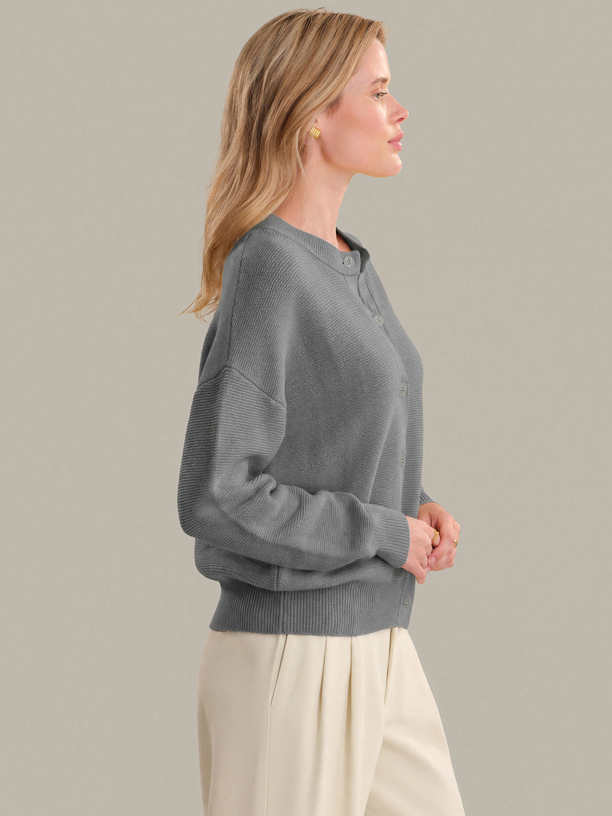 Woman wearing a gray sweater and beige pants against a plain background