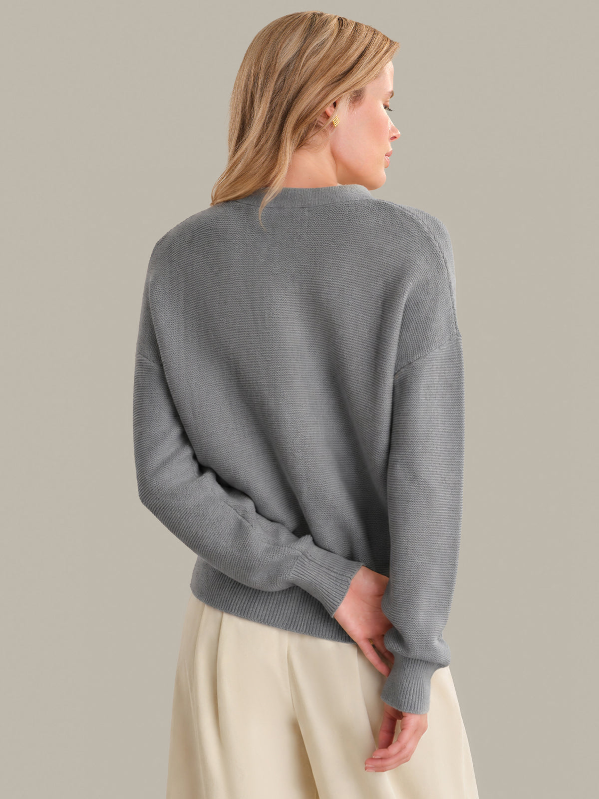 Woman wearing a gray sweater and beige pants against a plain background