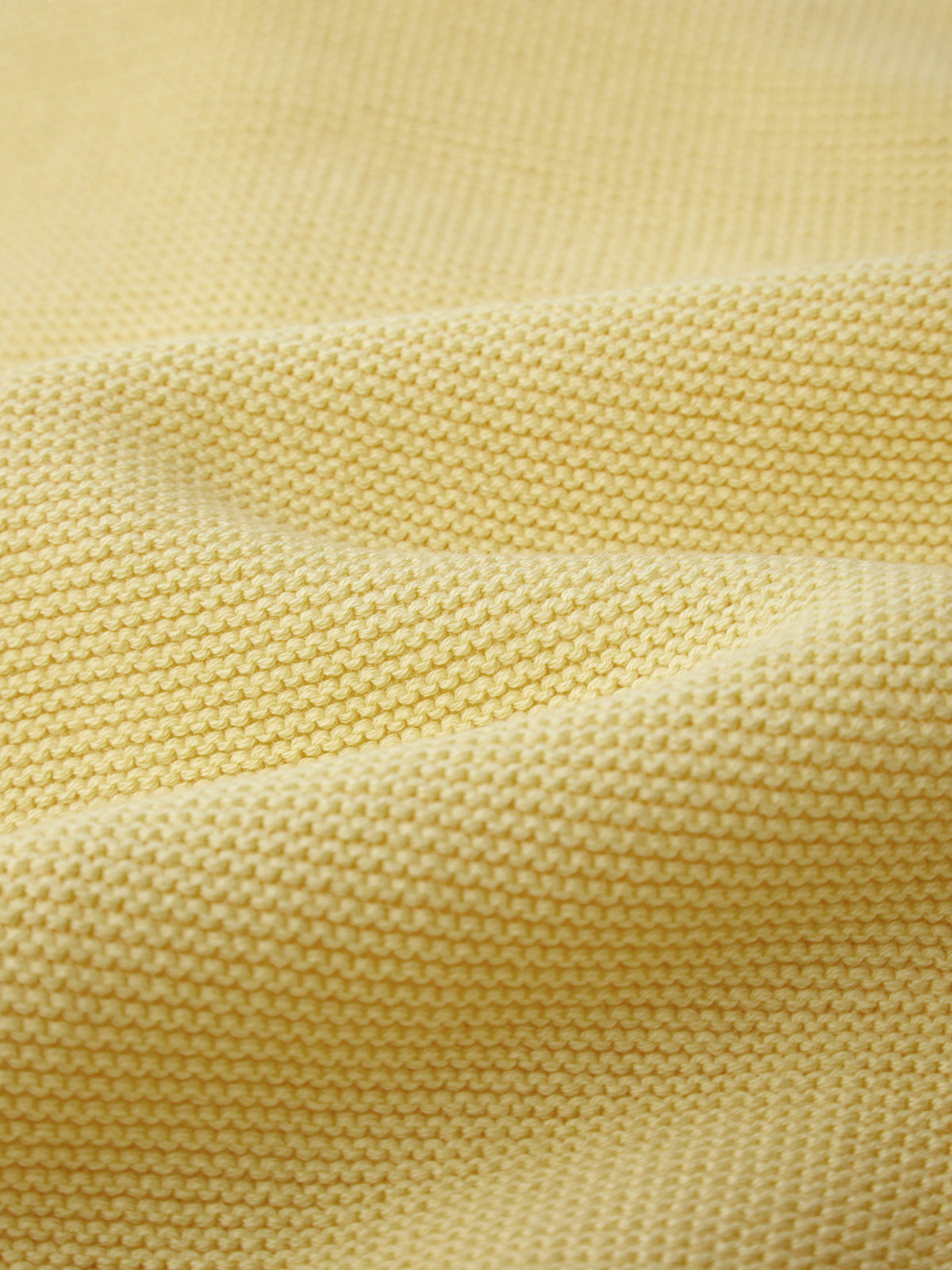 Close-up of a textured, yellow lightweight knit fabric by 525 America with visible horizontal rows and gentle folds, creating a soft wavy pattern—perfect for layering.