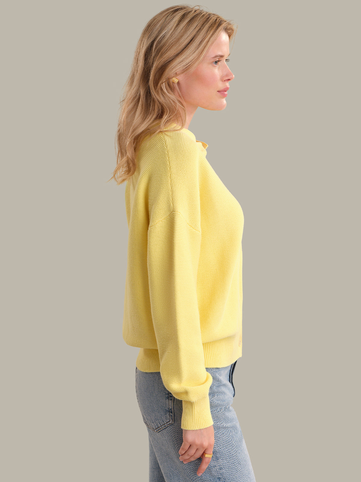Woman wearing a yellow sweater and blue jeans against a plain background