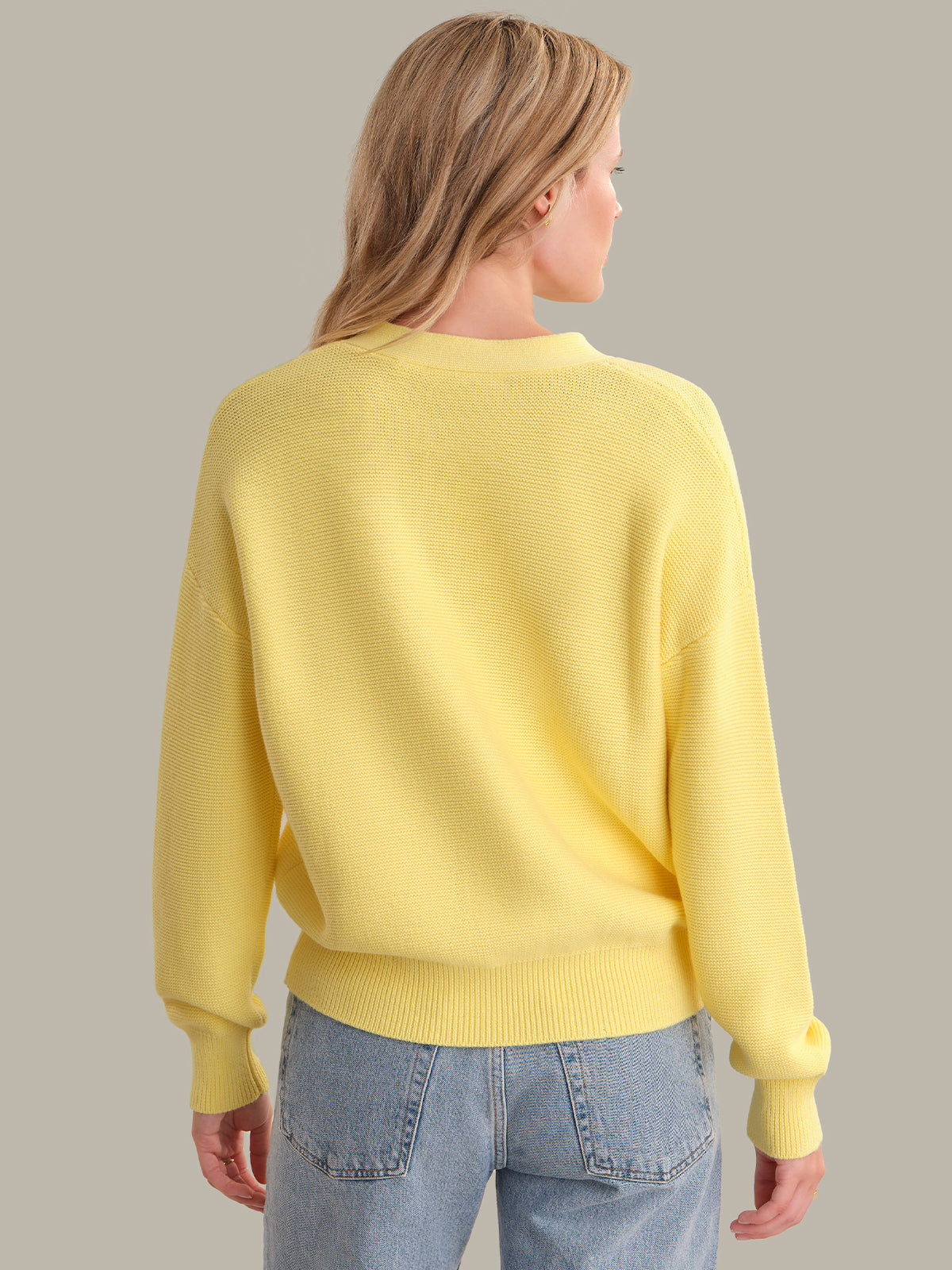 Person wearing a yellow sweater and blue jeans on a plain background