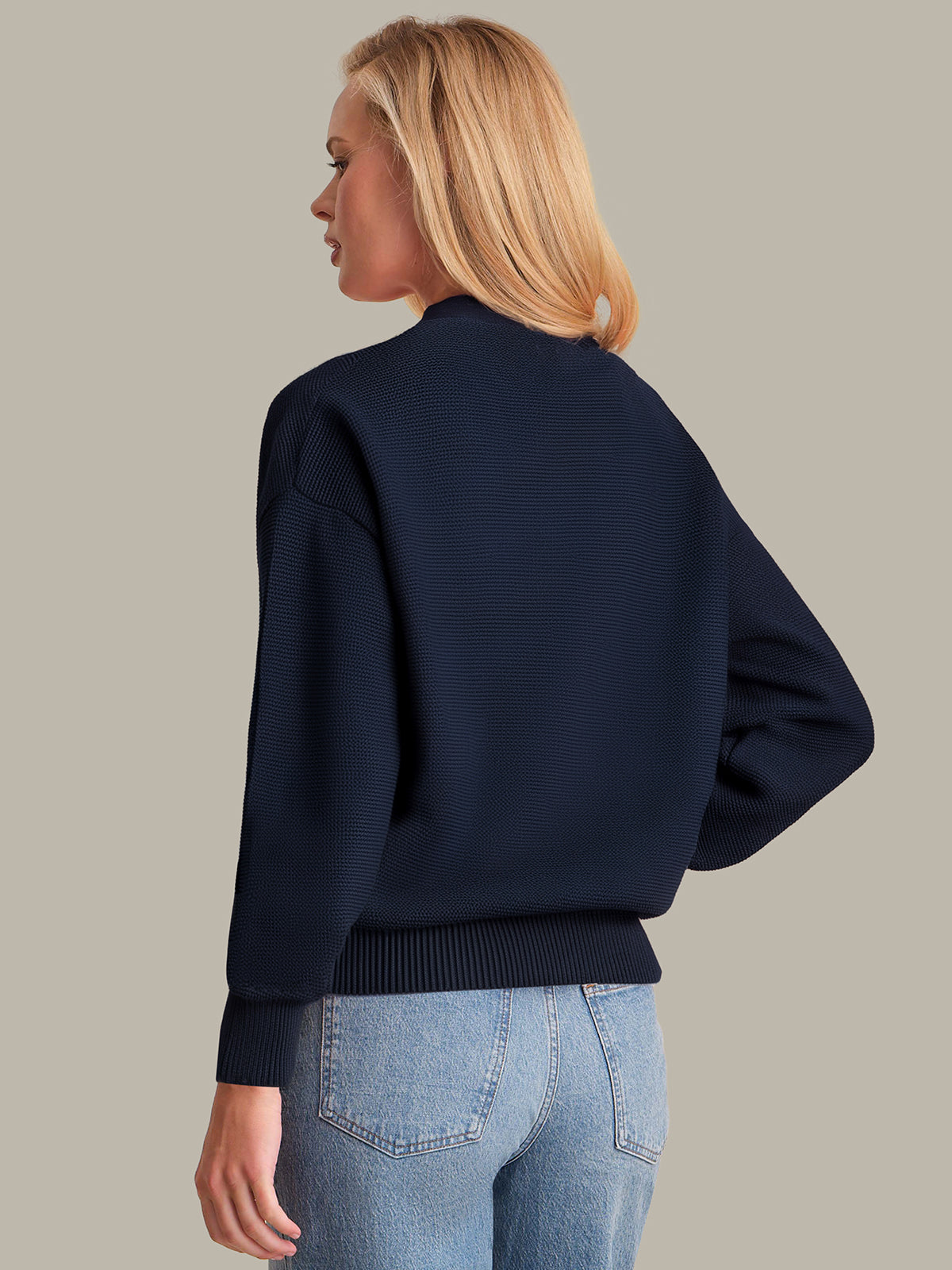 Person wearing a navy sweater and light blue jeans on a beige background