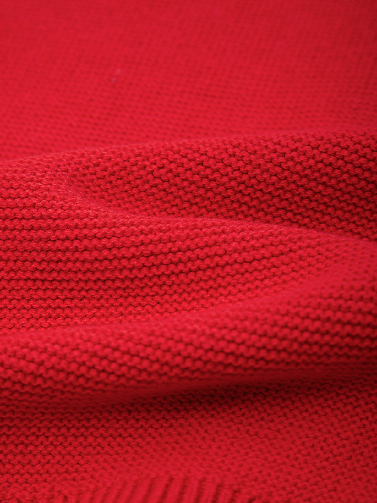 A close-up of bright red knit fabric with a textured ribbed pattern and soft folds.