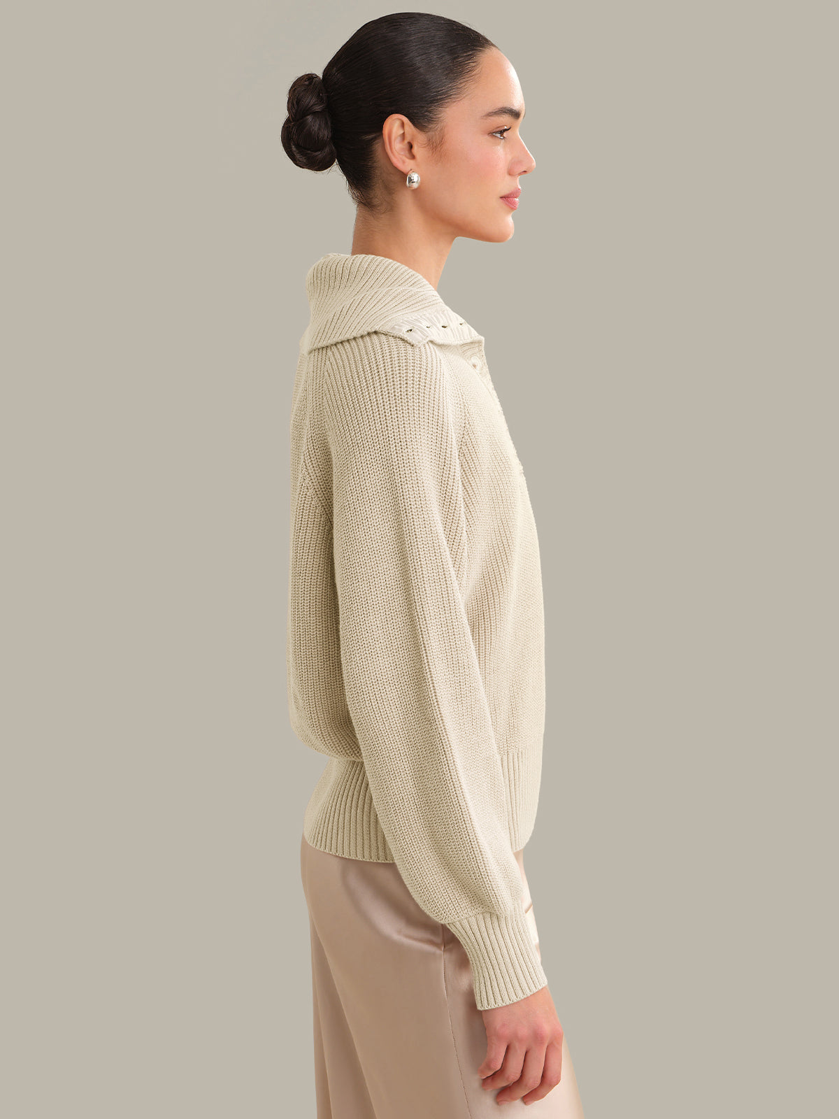Woman wearing a beige sweater with a collar against a plain background