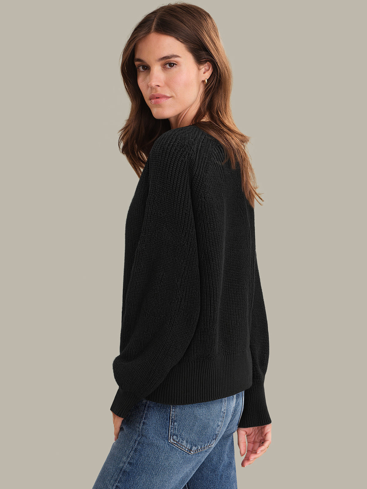 Woman wearing a black sweater and blue jeans on a plain background