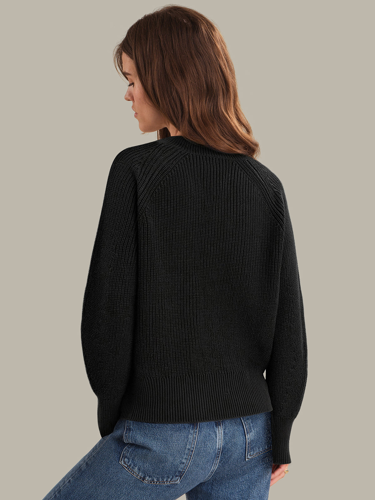 Woman wearing a black sweater and blue jeans against a neutral background
