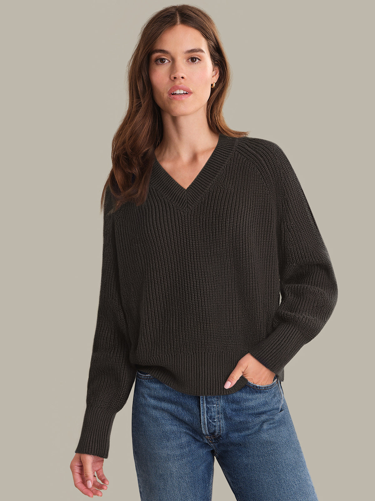 Woman wearing a brown sweater and blue jeans against a neutral background