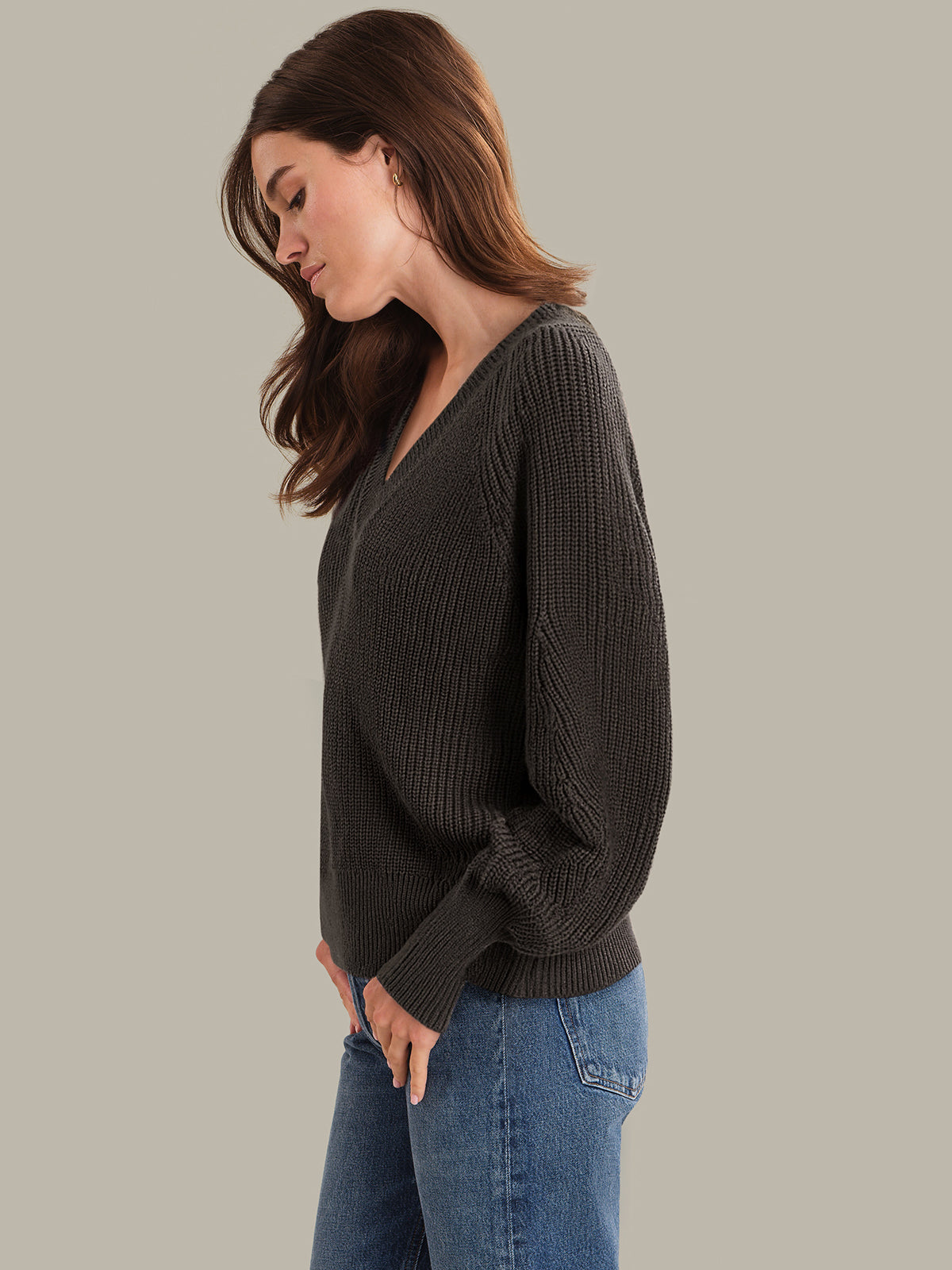Woman wearing a brown sweater and blue jeans against a plain background