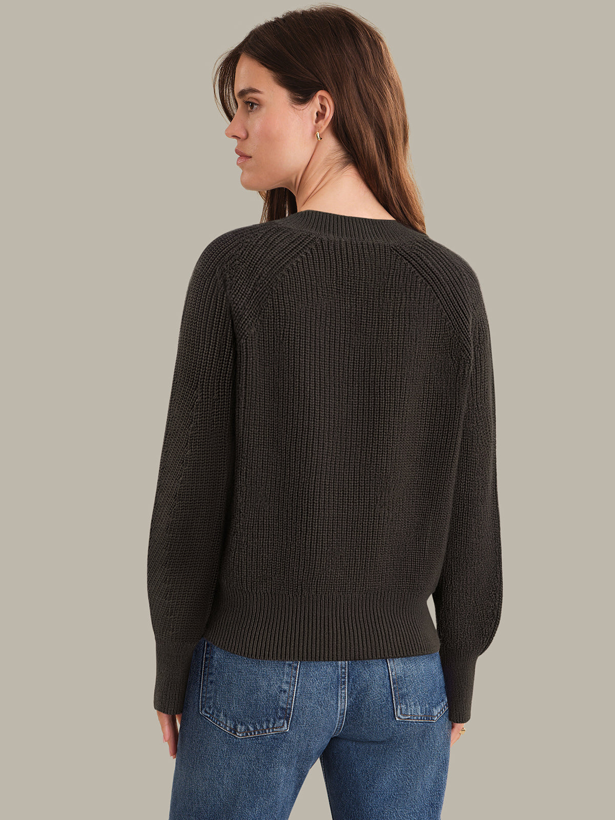 Woman wearing a brown sweater and blue jeans against a plain background