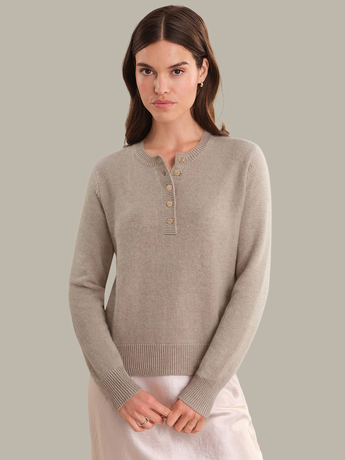 Woman wearing a beige sweater with button details against a plain background