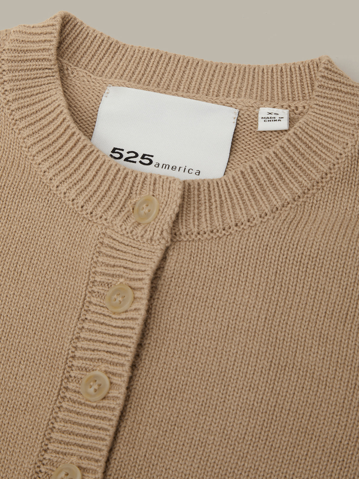 Close-up of a brown cardigan with a visible brand label on a neutral background