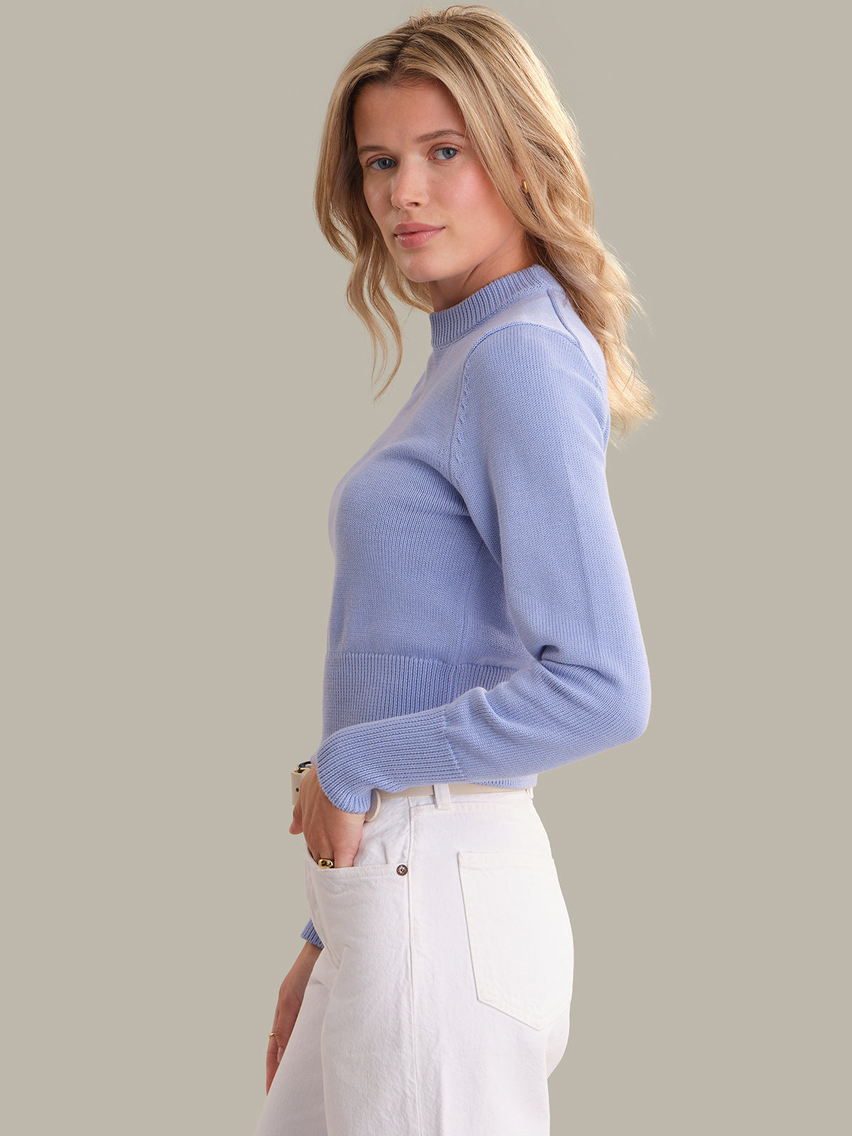 Woman wearing a light blue sweater and white pants against a plain background