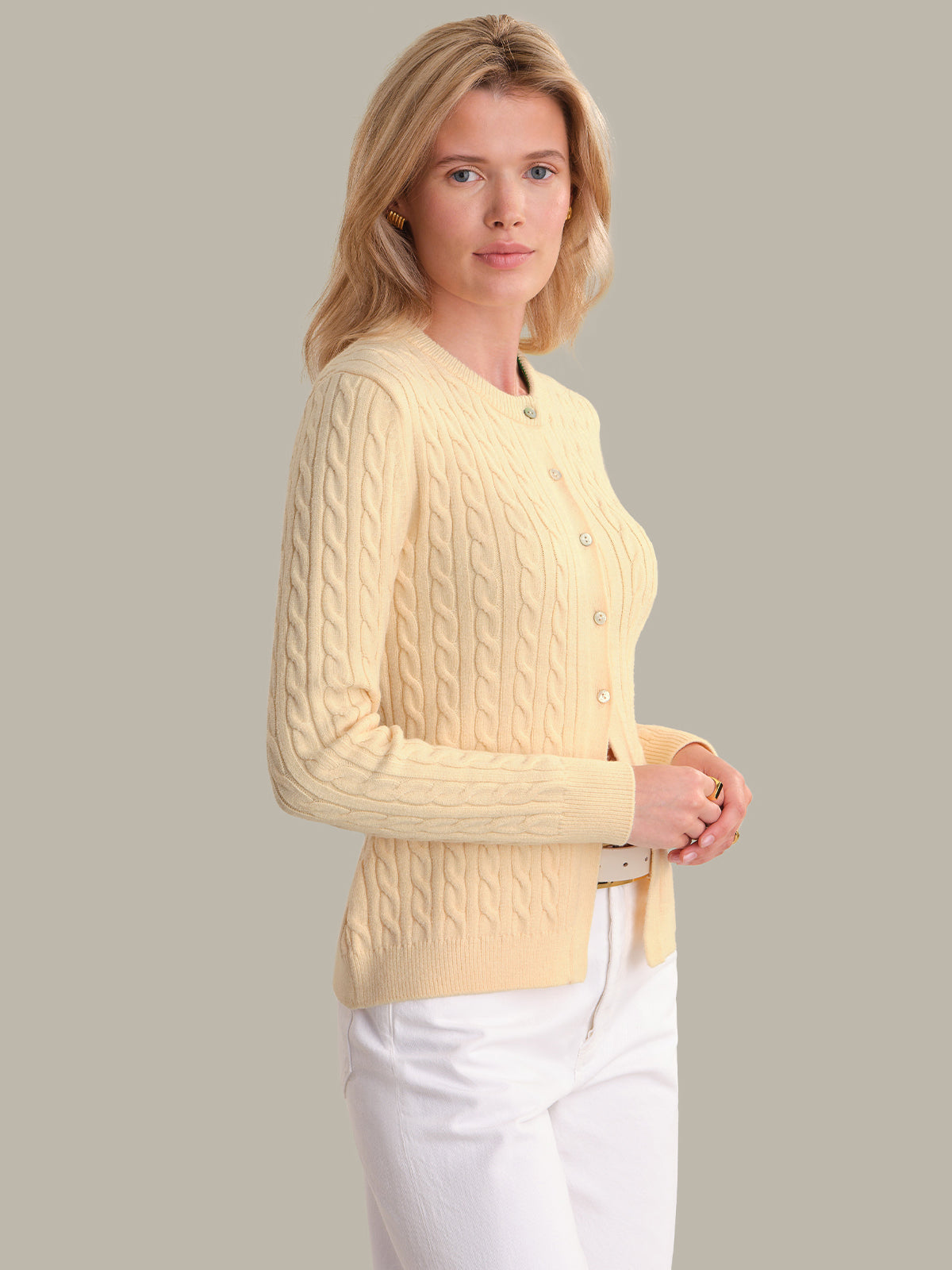 Woman wearing a light yellow cable knit cardigan against a plain background