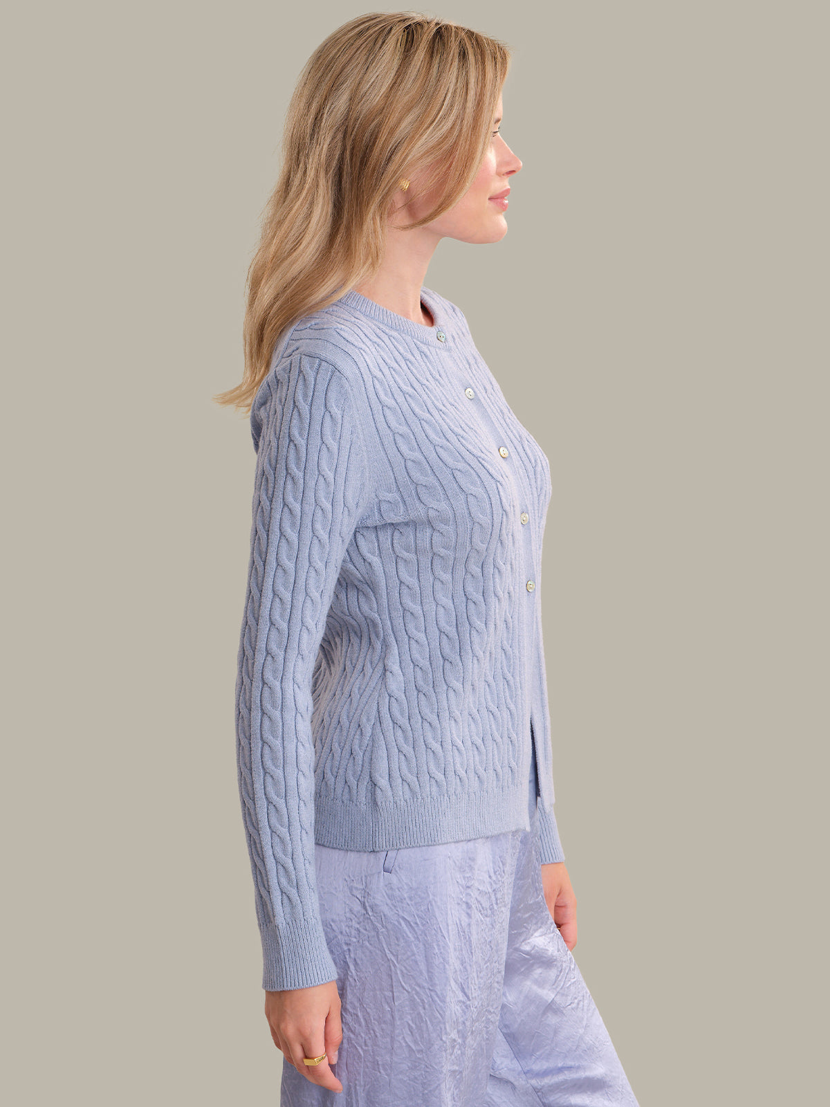 Woman wearing a light blue cable knit sweater and pants on a plain background