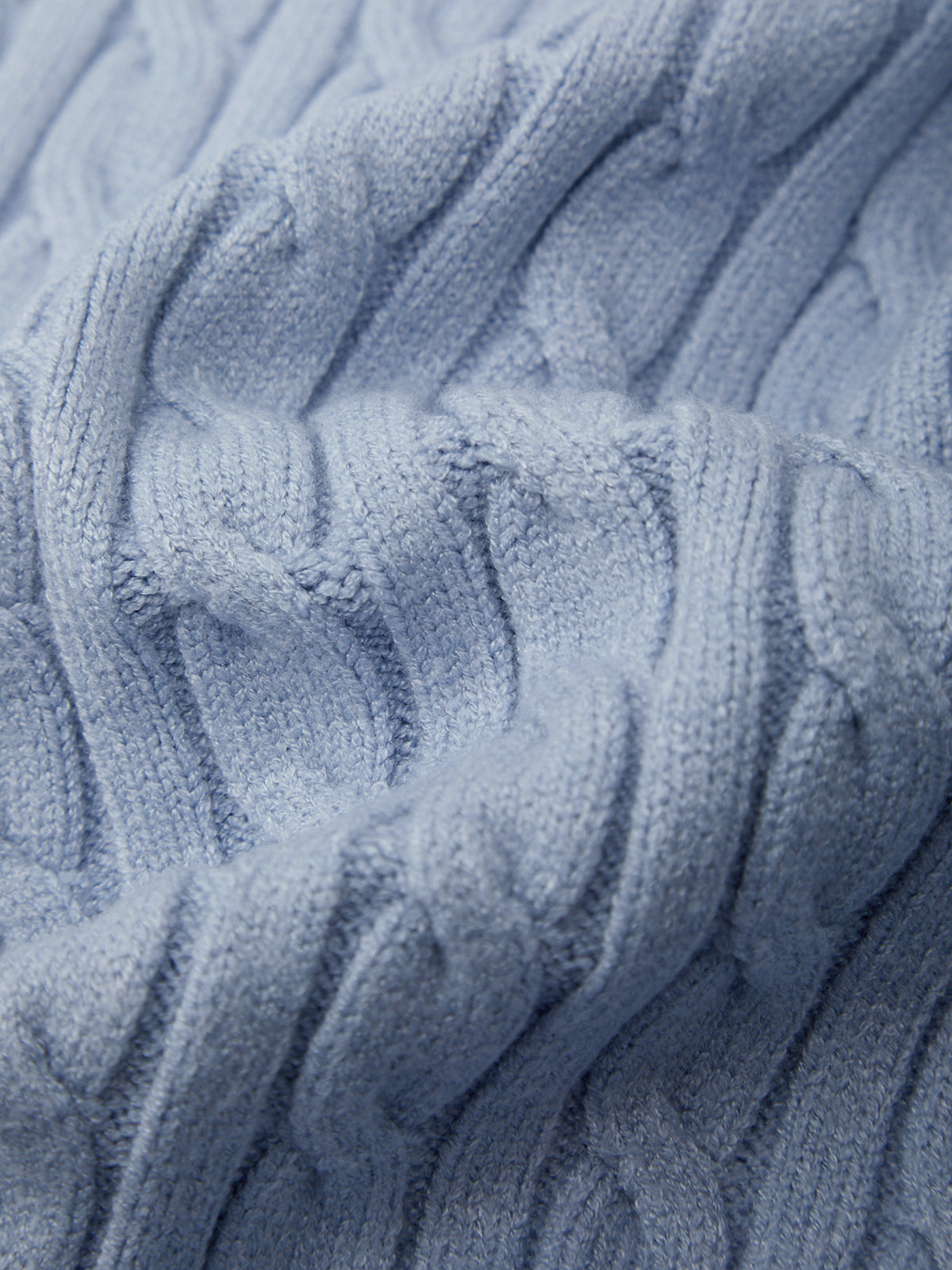 A close-up of a light blue cable-knit fabric texture, showing the detailed knit pattern and soft folds.