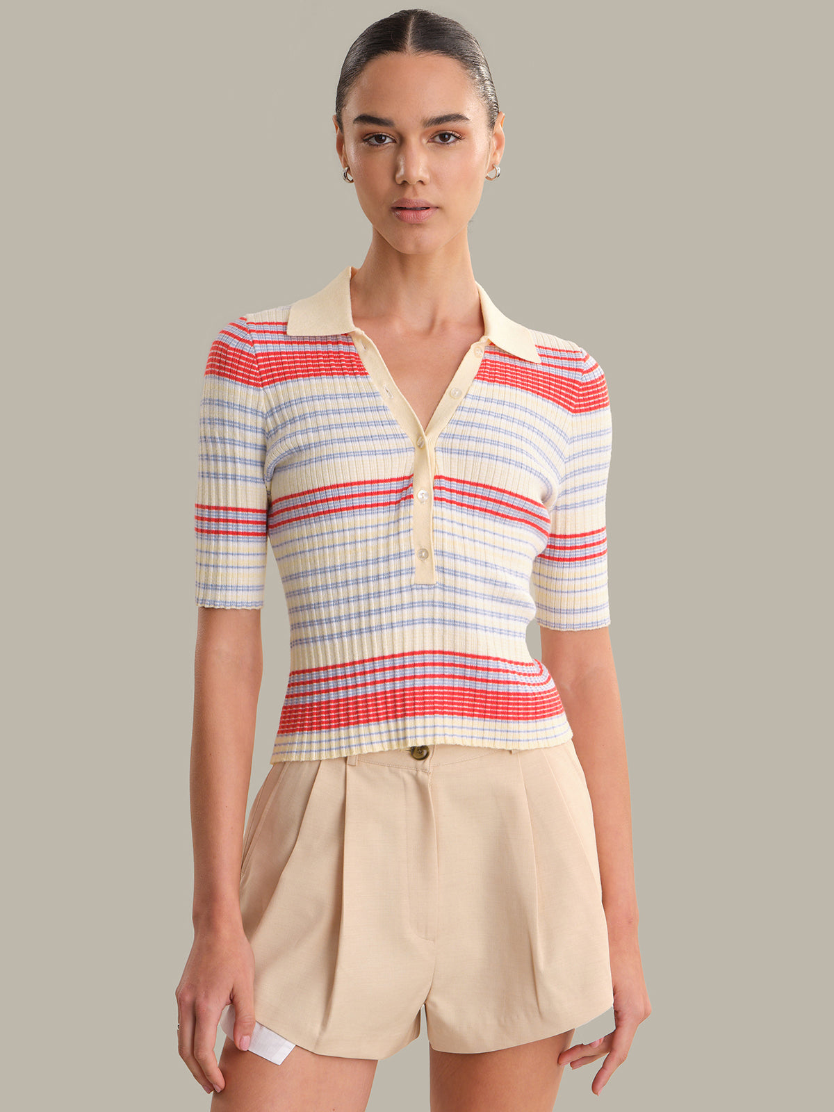 Woman wearing a colorful striped shirt and beige shorts against a gray background
