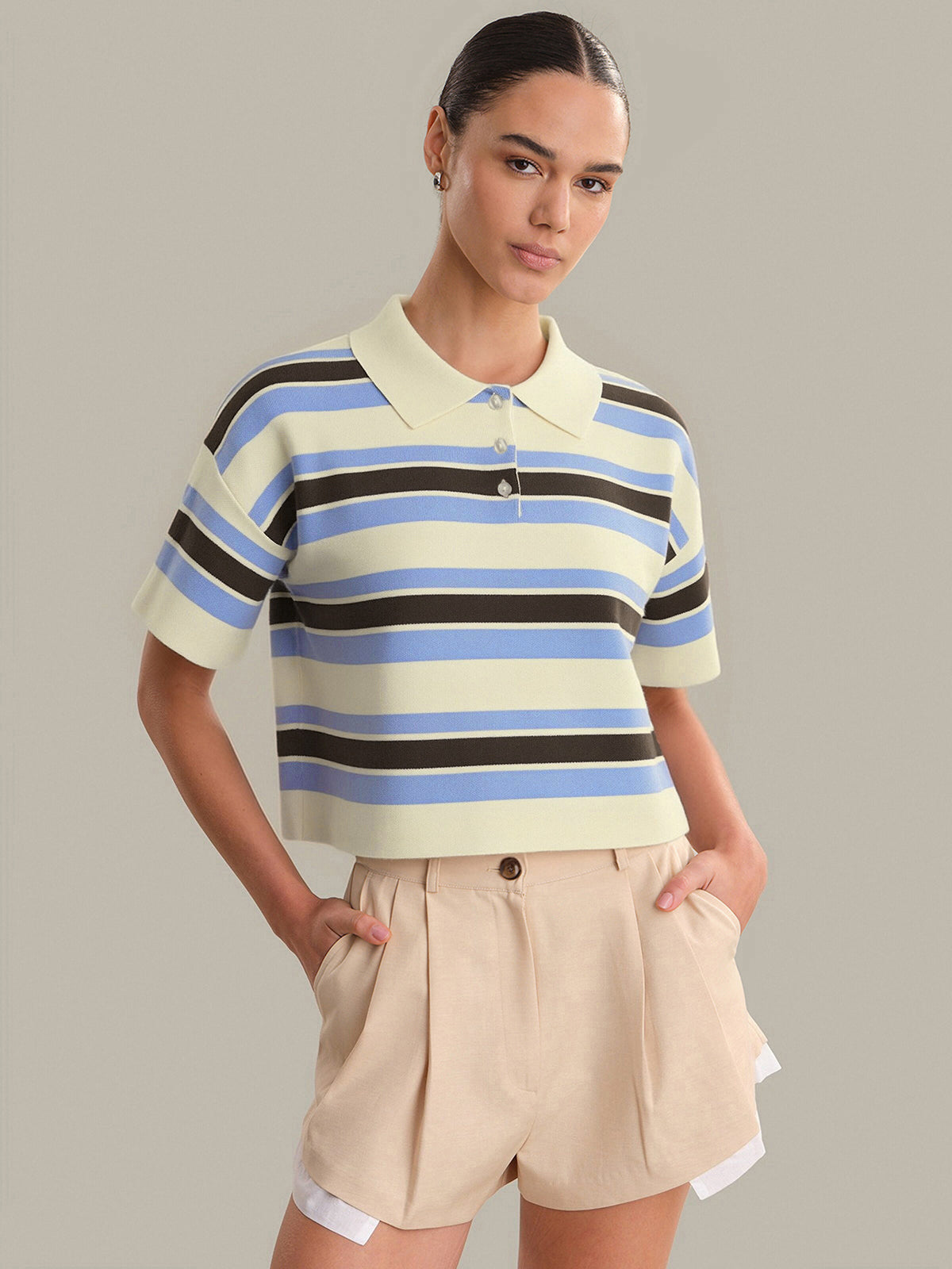 Woman wearing a striped polo shirt and beige shorts against a gray background