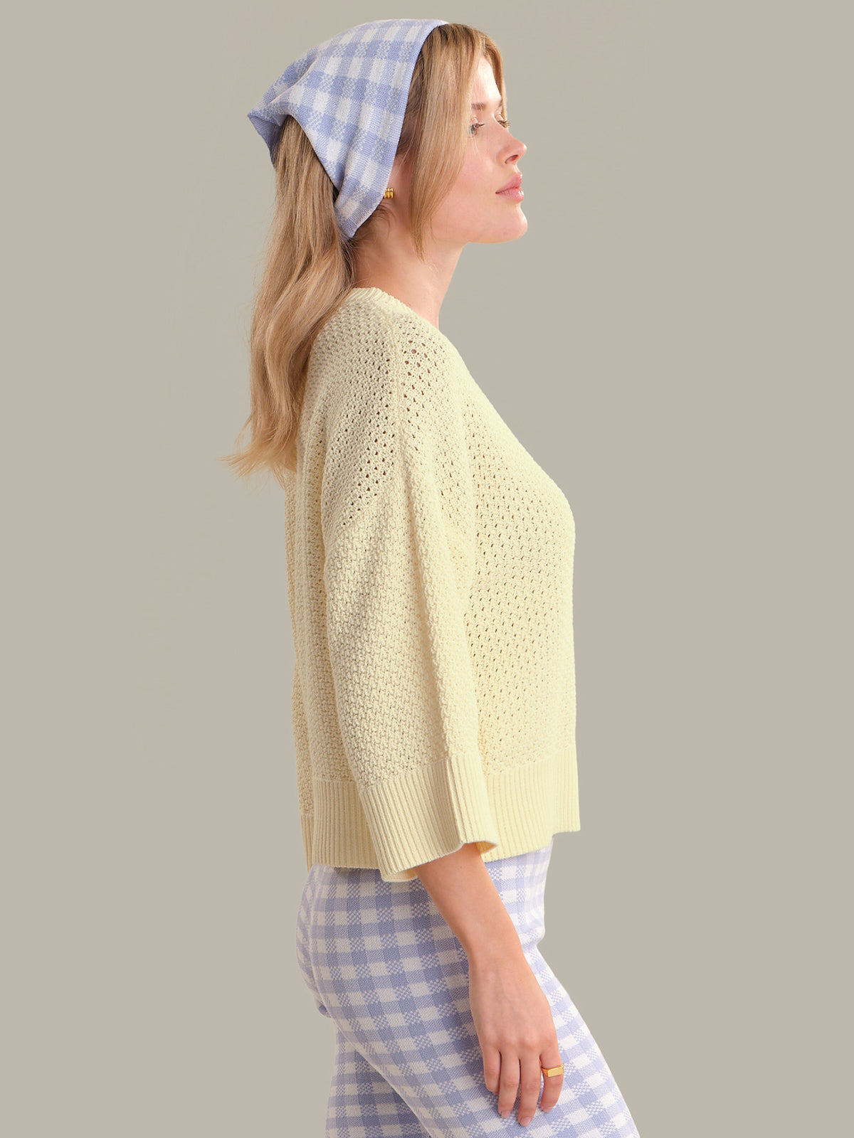 Woman wearing a light yellow top and blue checkered headscarf on a plain background