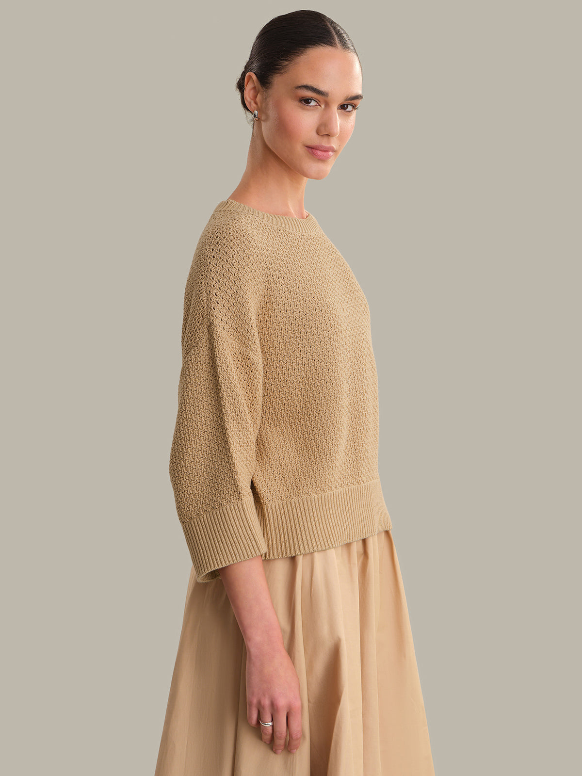 Woman wearing a beige sweater and skirt against a neutral background