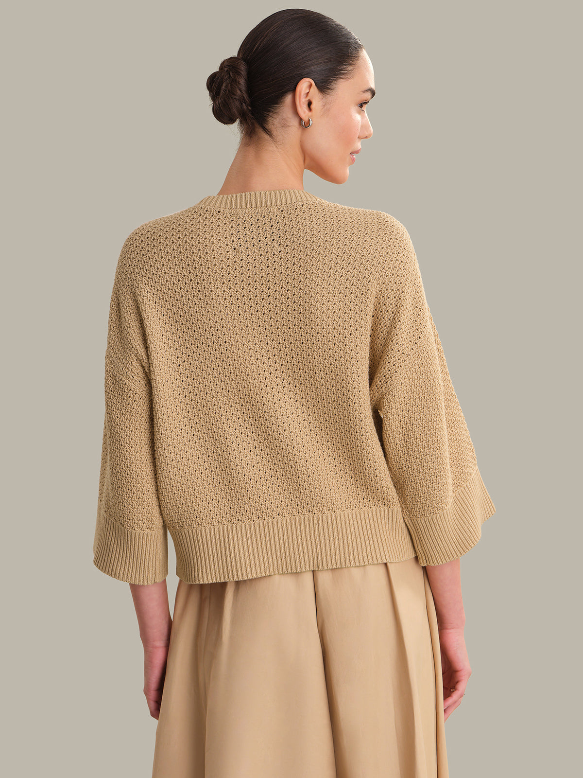 Woman wearing a beige knitted sweater and pants against a neutral background