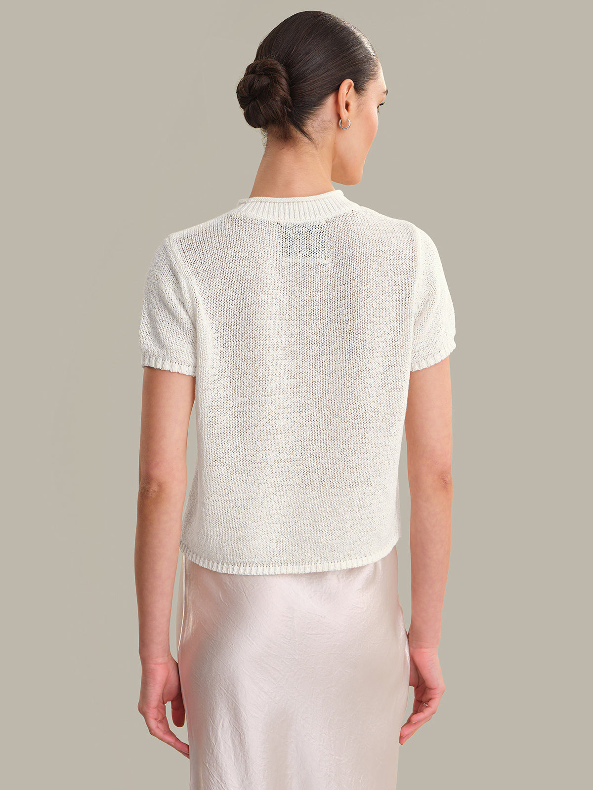 Woman wearing a white knit top against a neutral background
