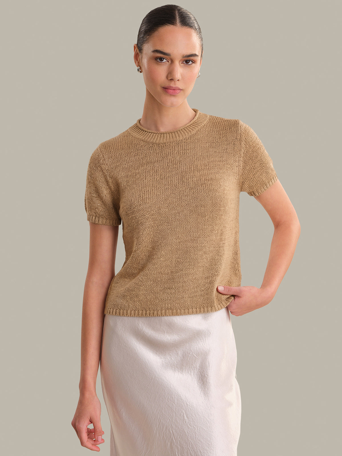 Woman wearing a beige knit top against a neutral background