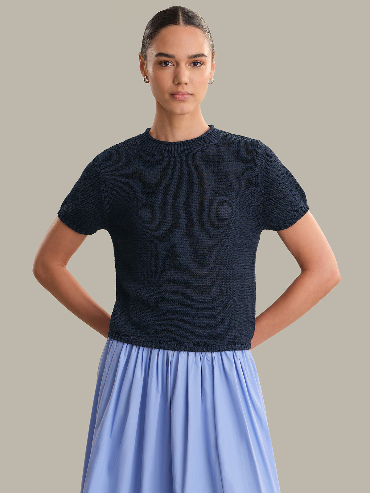 Woman wearing a navy sweater and light blue skirt against a neutral background