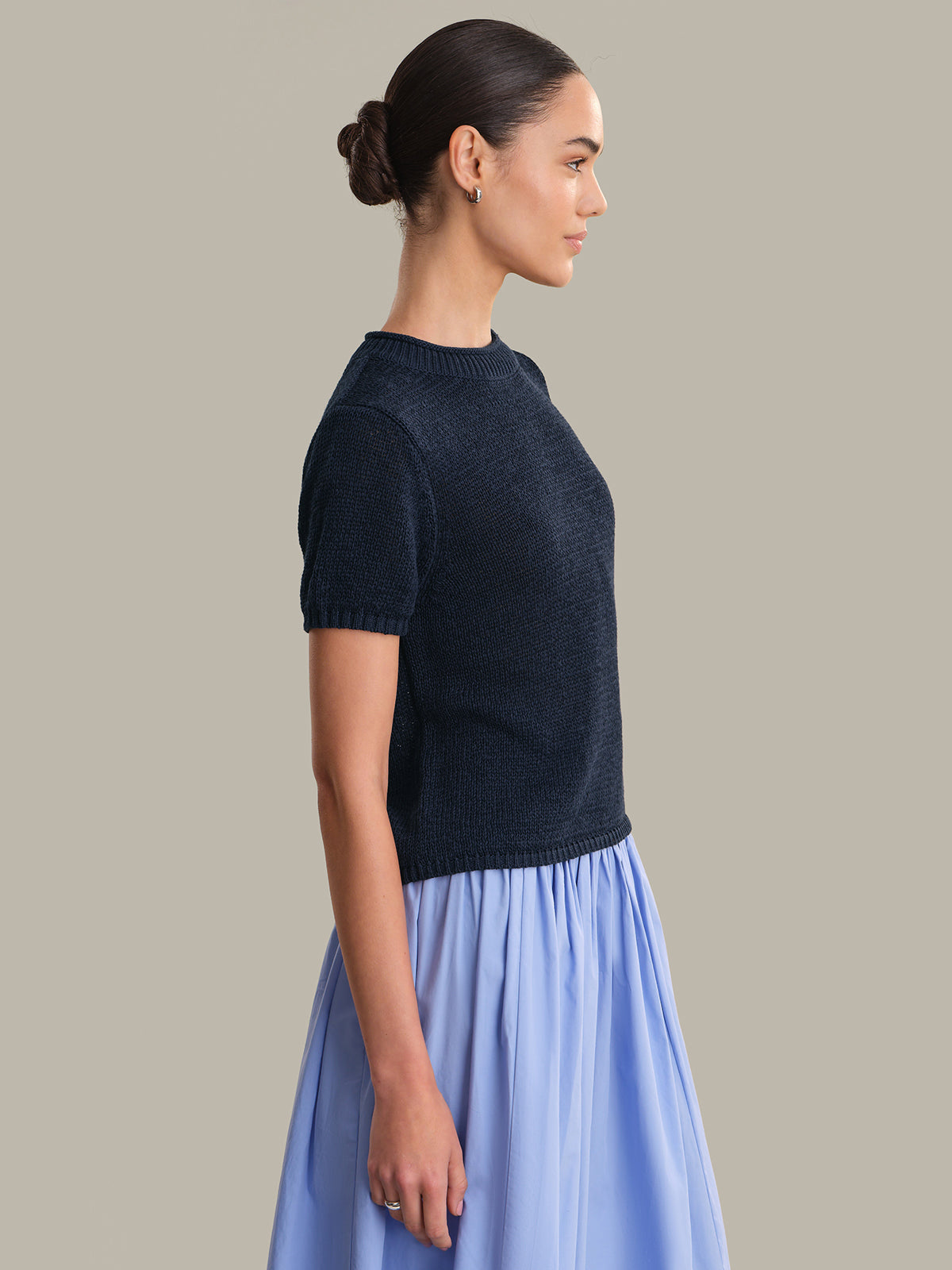 Woman wearing a dark blue knitted top and light blue skirt against a beige background
