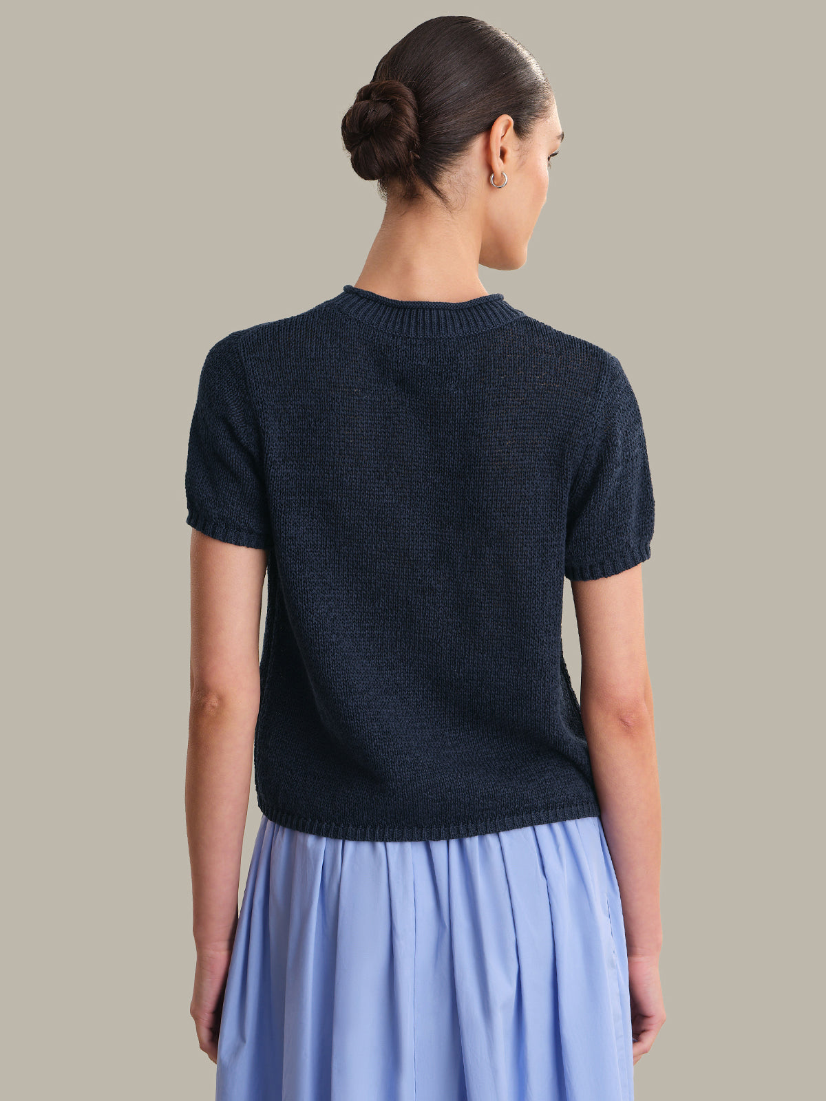 Woman wearing a dark blue short-sleeve top and light blue skirt on a neutral background