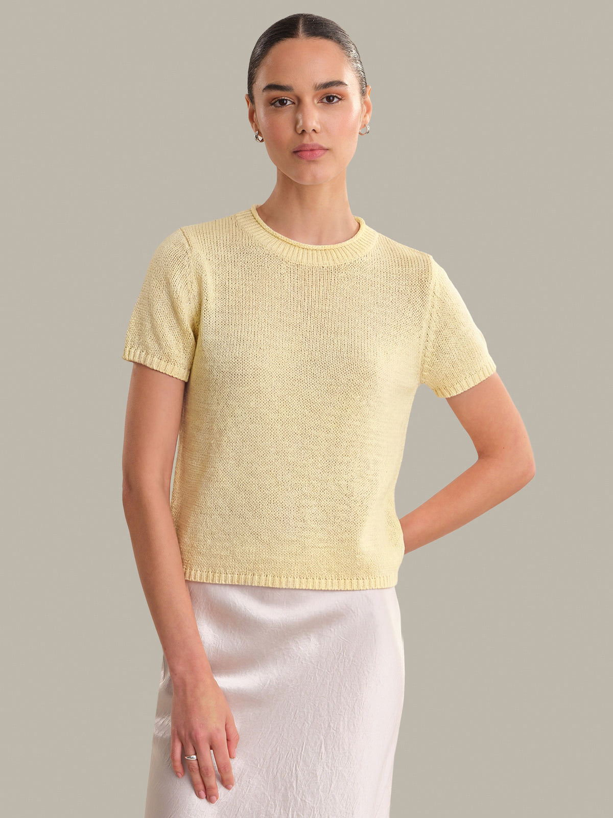 Woman wearing a yellow knit top and white skirt against a gray background
