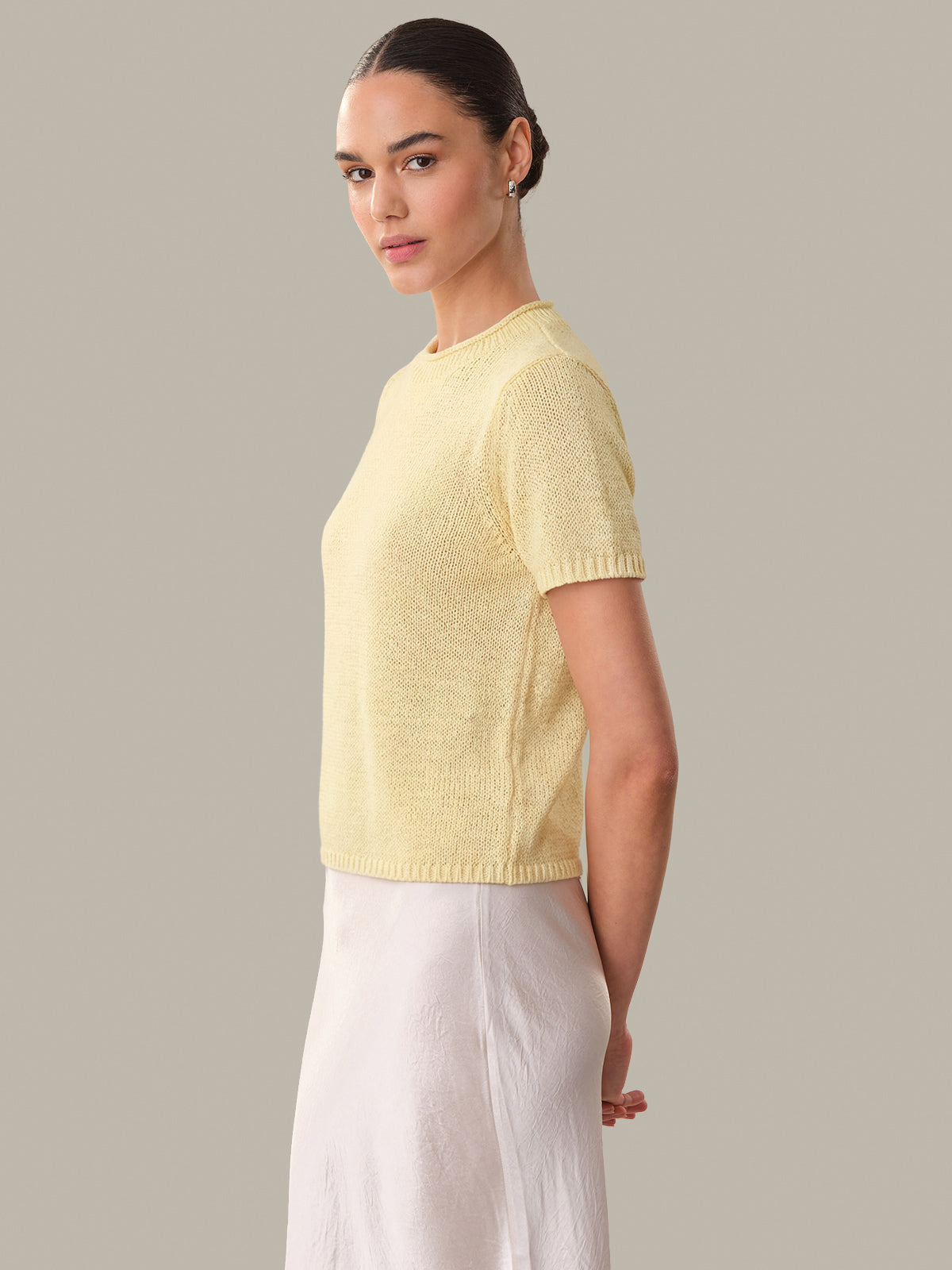 Woman wearing a light yellow knitted sweater and white pants against a neutral background