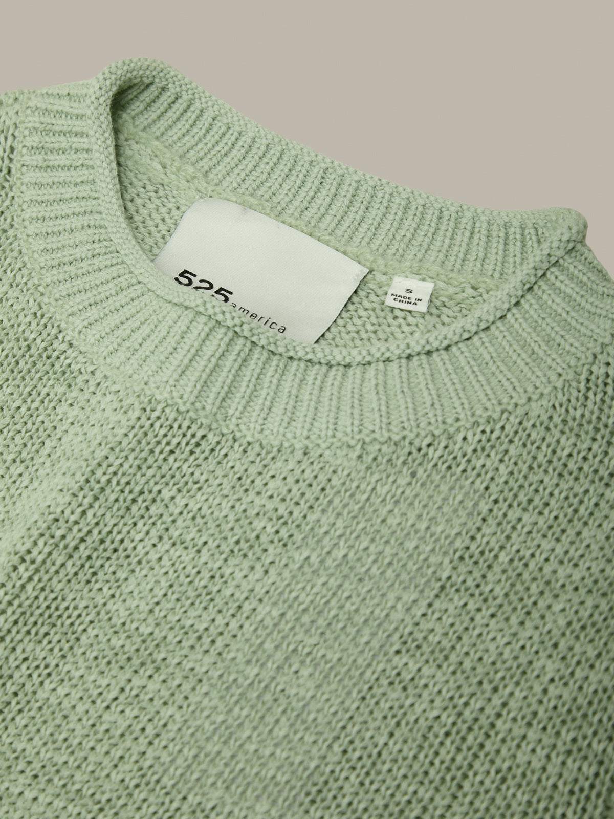 Close-up of a green knit sweater with a brand label on a beige background